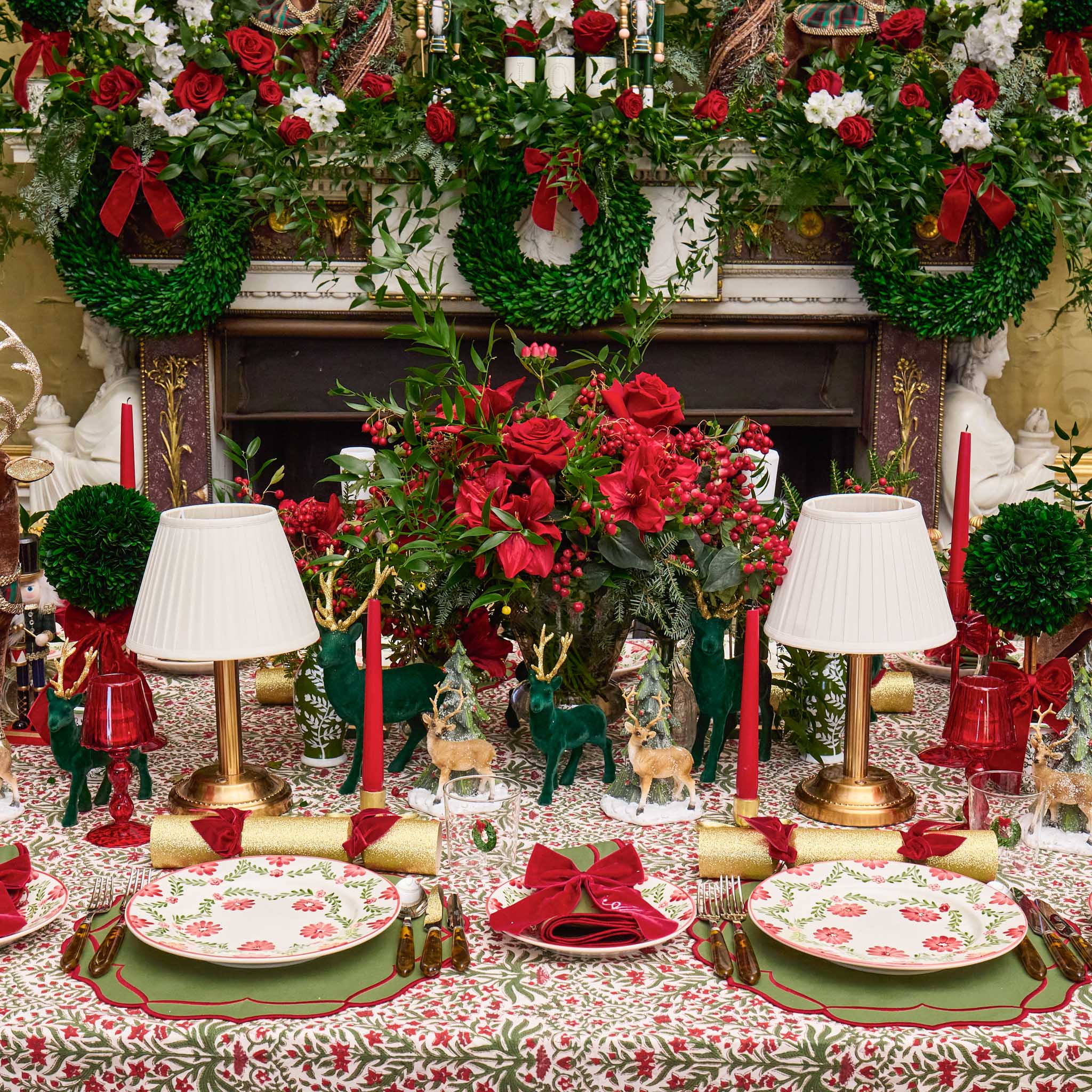 Decorative Christmas table setting with red and green floral arrangements, candles, and tableware.