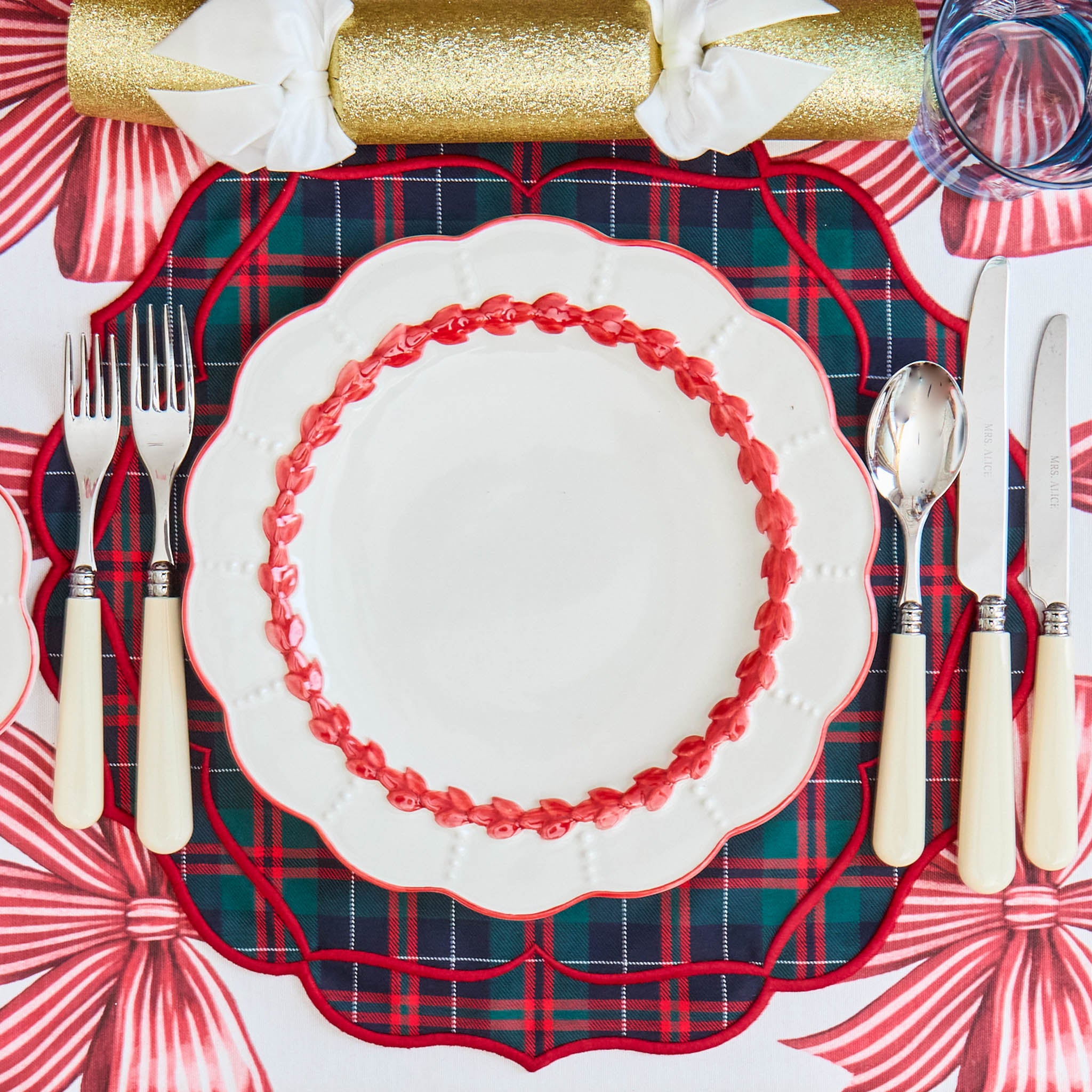 Christmas-themed table setting with red and green plaid placemat, white plate with red rim, and decorative elements.
