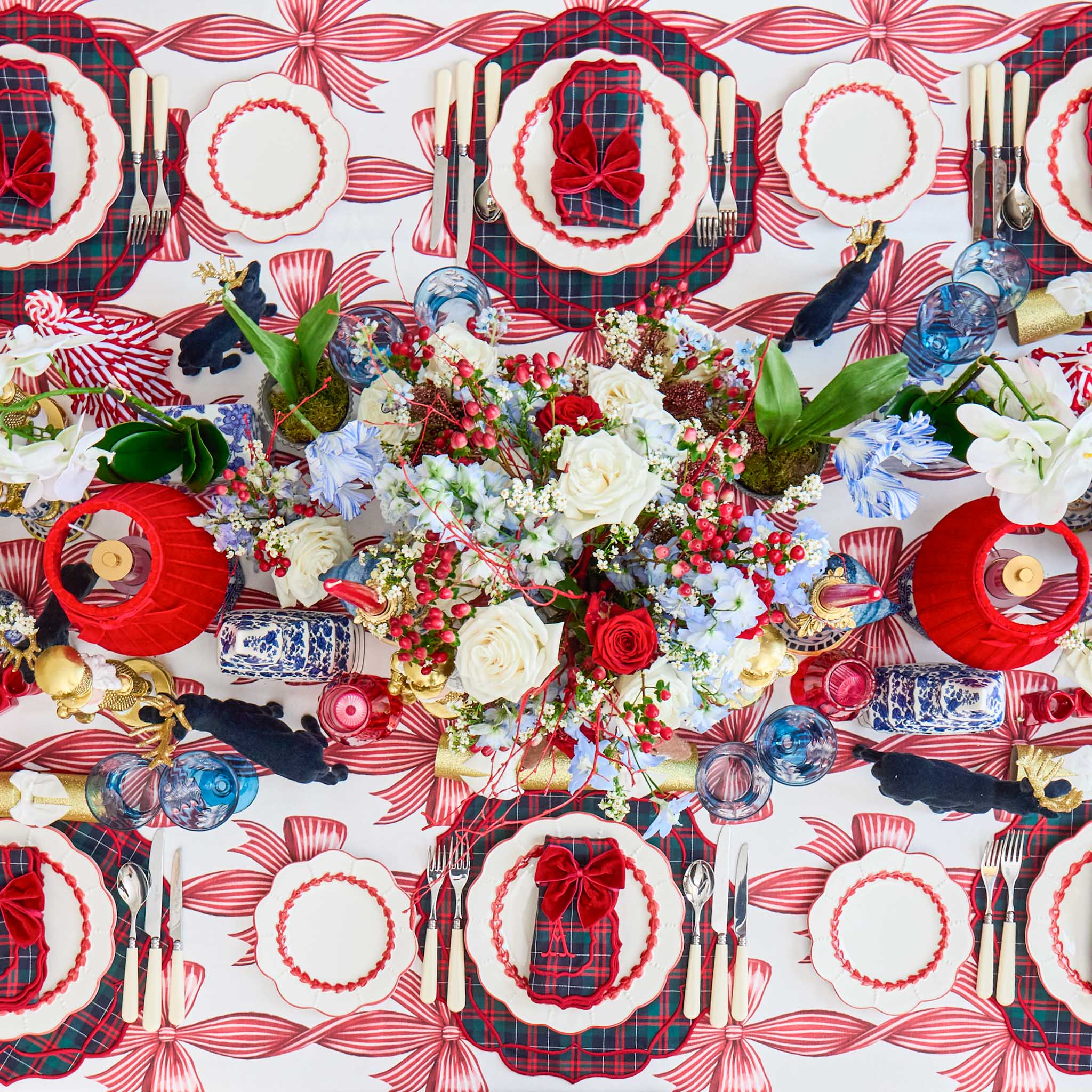 Decorative Christmas table setting with red and white tablecloth, plaid napkins, and floral centerpieces.