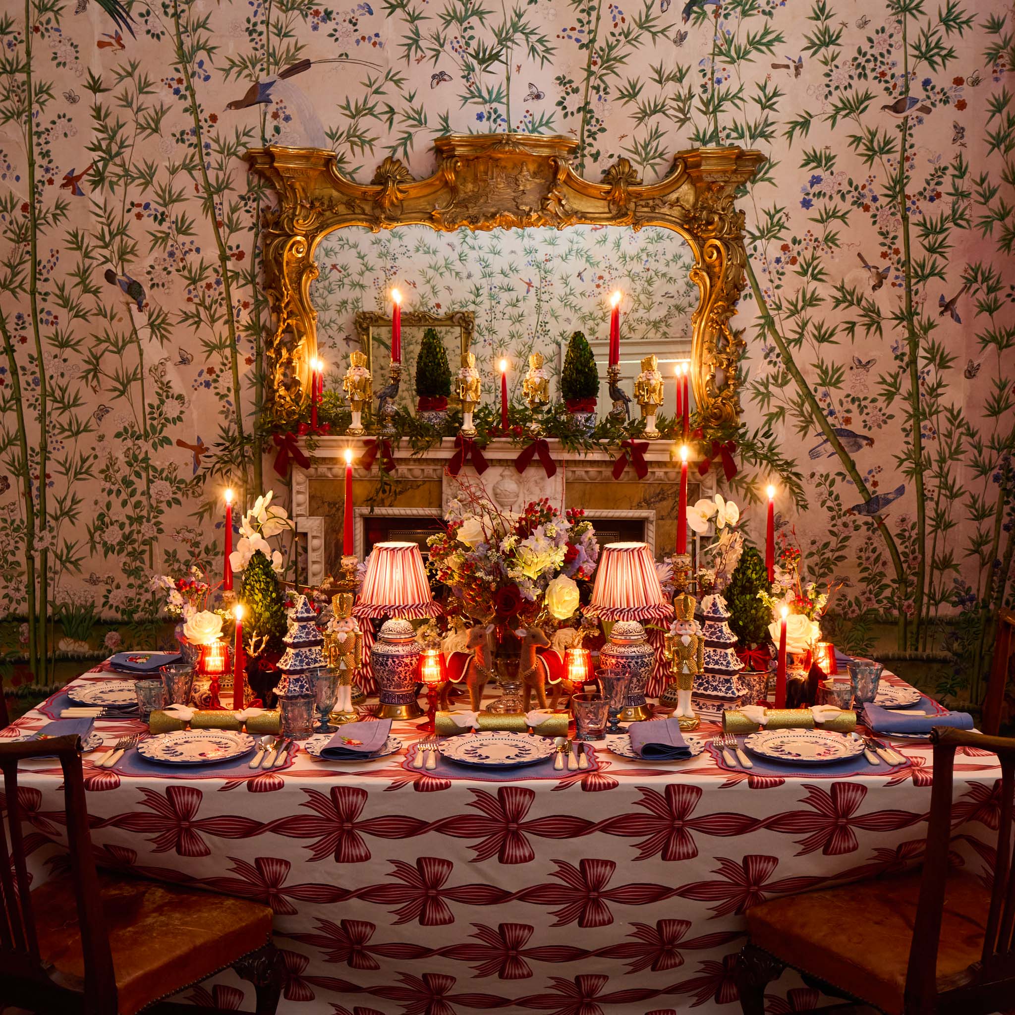 Decorative table setting with candles and floral arrangements in a room with floral wallpaper and a large mirror.