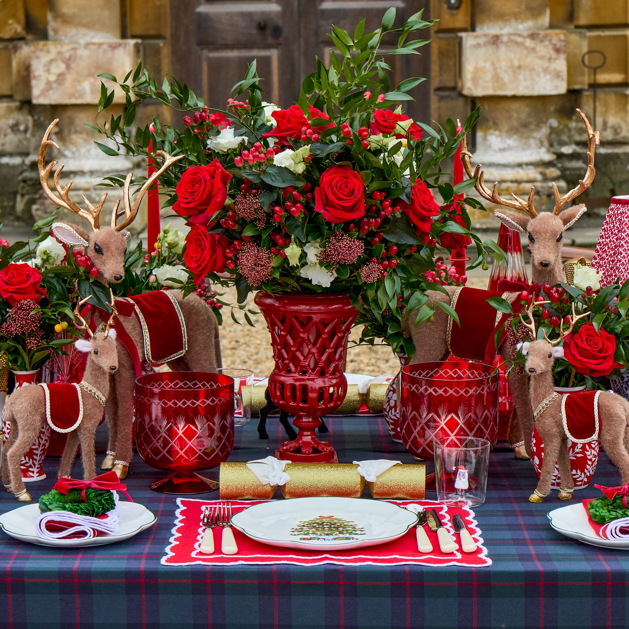 Decorative Christmas table setting with red roses, reindeer figurines, and plaid tablecloth.