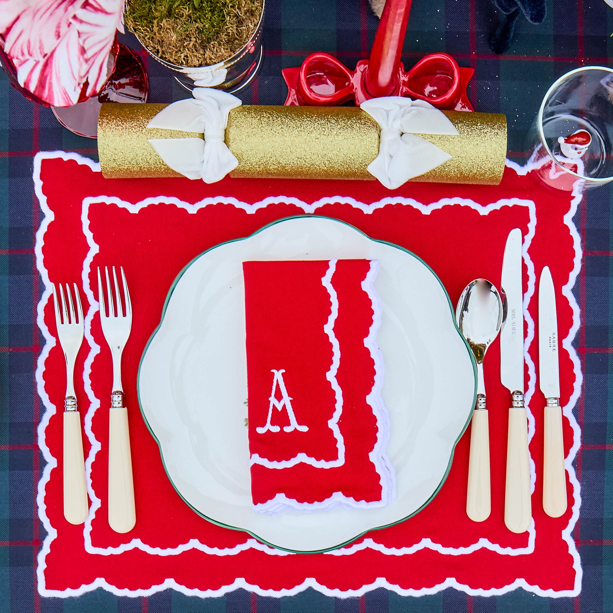 Decorative table setting with a red napkin, white plate, and cutlery on a blue plaid tablecloth.