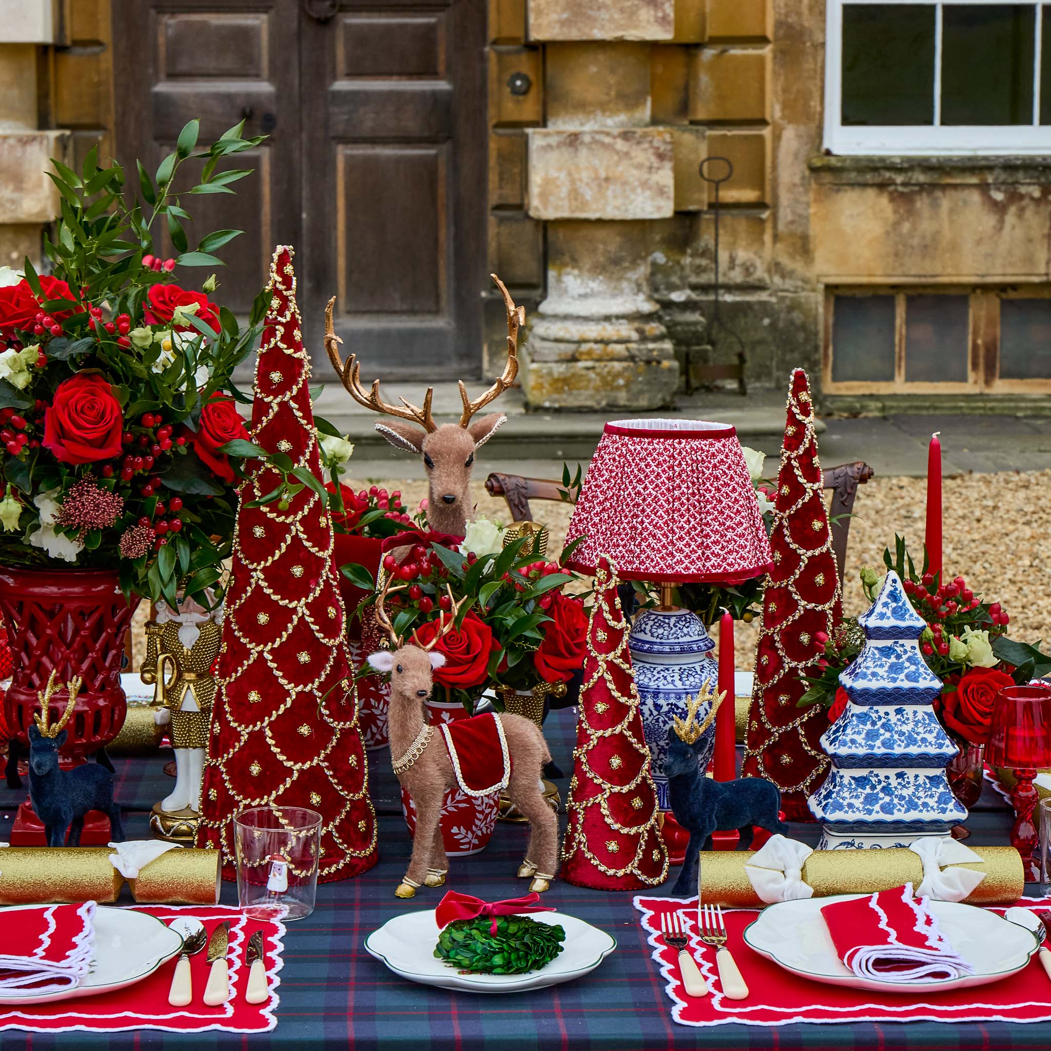 Decorative Christmas table setting with trees, reindeer, and candles in front of a building.