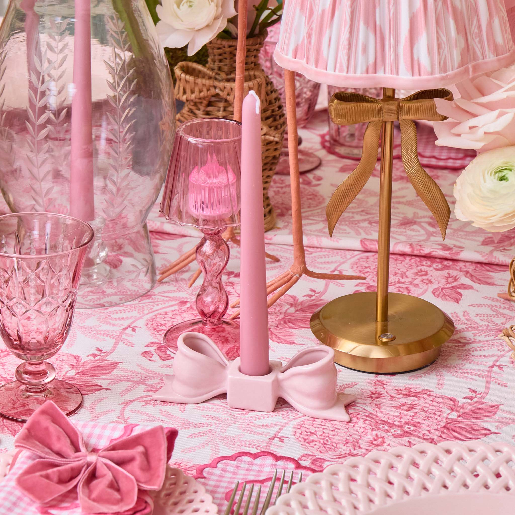 Pink candle holder with decorative bow on a tablecloth with floral pattern