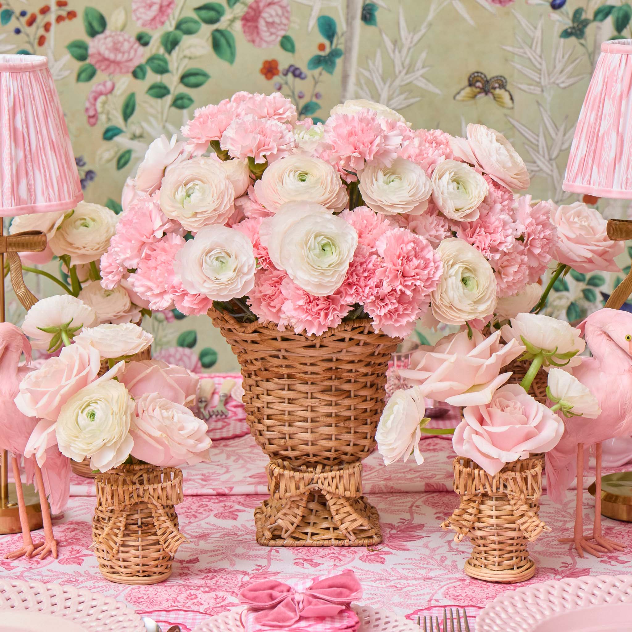 Decorative setup with pink and white flowers in wicker vases on a patterned tablecloth.