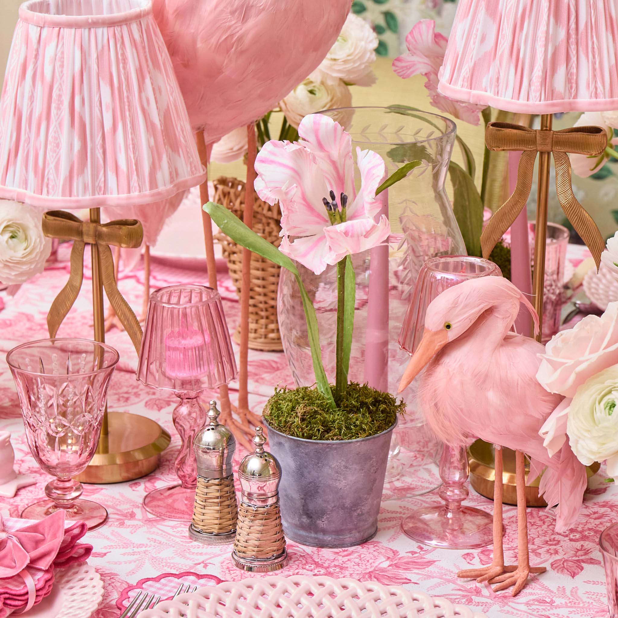 Pink flamingo, table lamps, and decorative items on a table with a floral tablecloth.