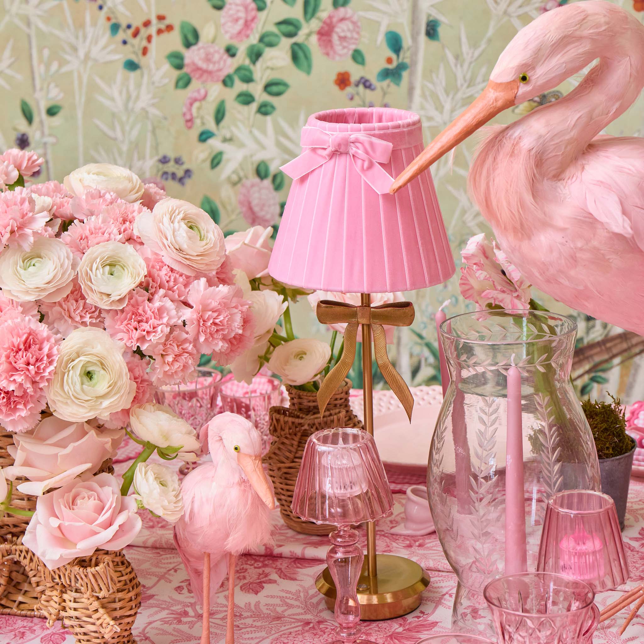 Pink flamingo decor with floral arrangements and table settings on a floral wallpaper background