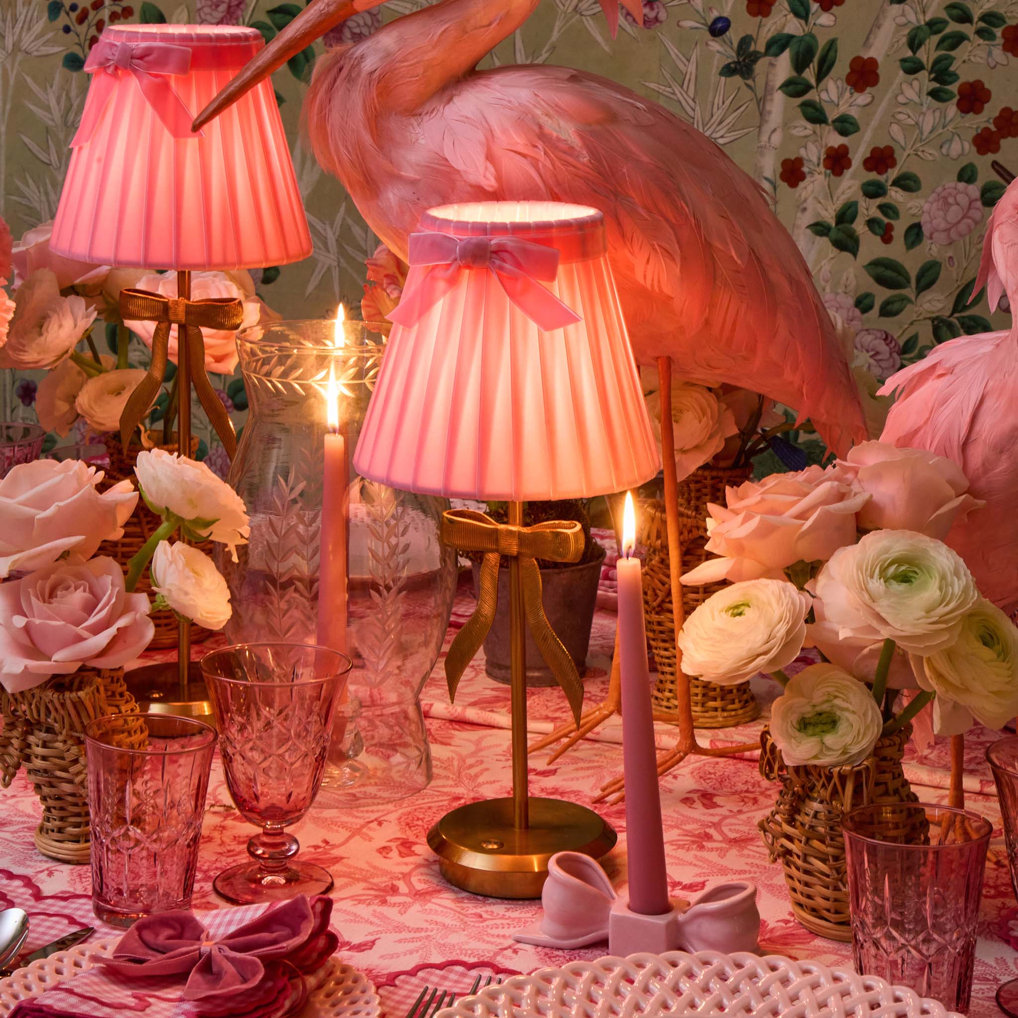 Decorative table setting with pink flamingo lamps, flowers, and candles on a patterned tablecloth.