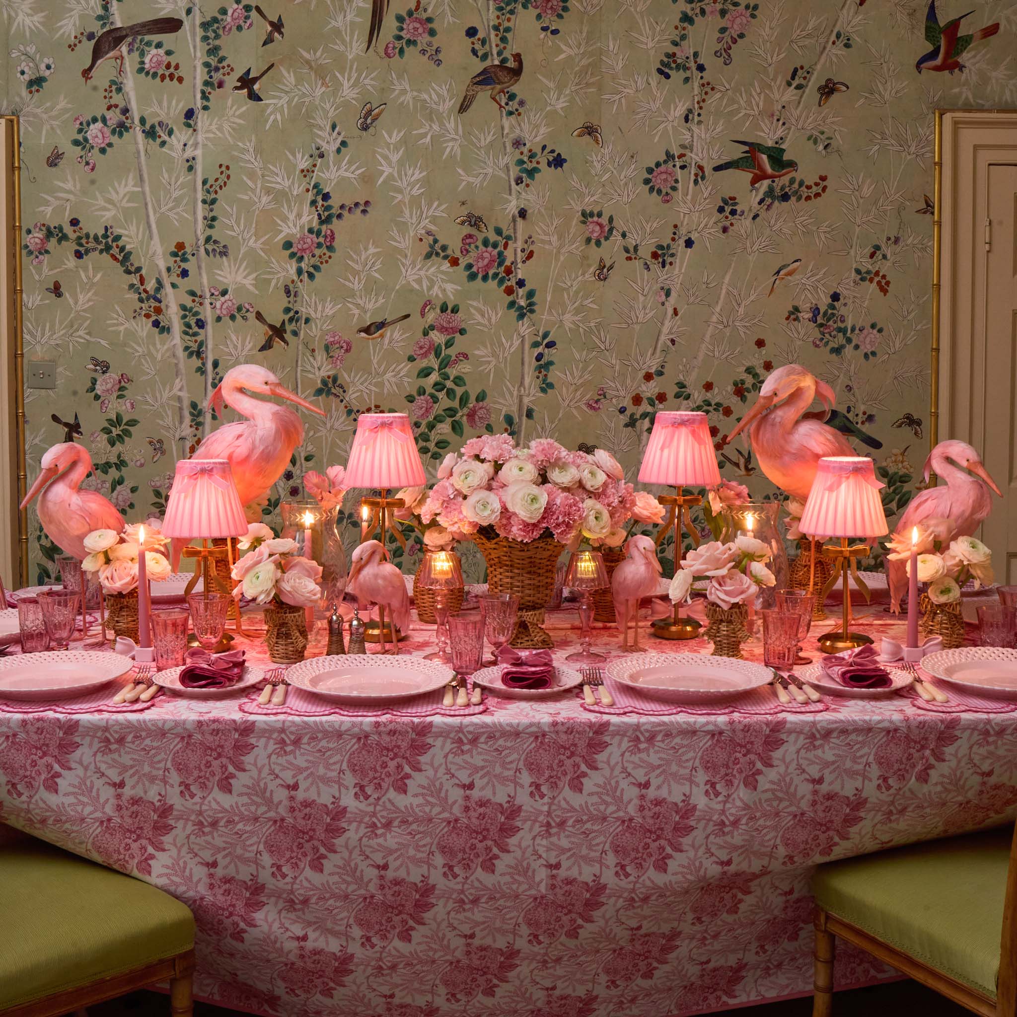 Decorative table setting with pink flamingo figurines, floral arrangements, and patterned tablecloth.