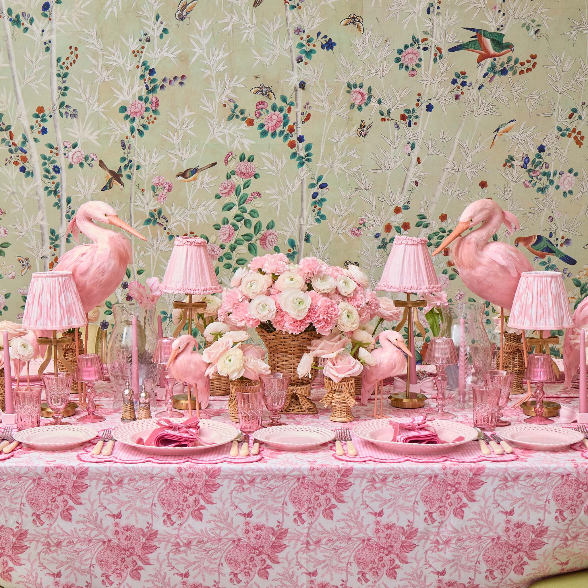 Decorative table setting with pink flamingo decorations against a floral wallpaper background