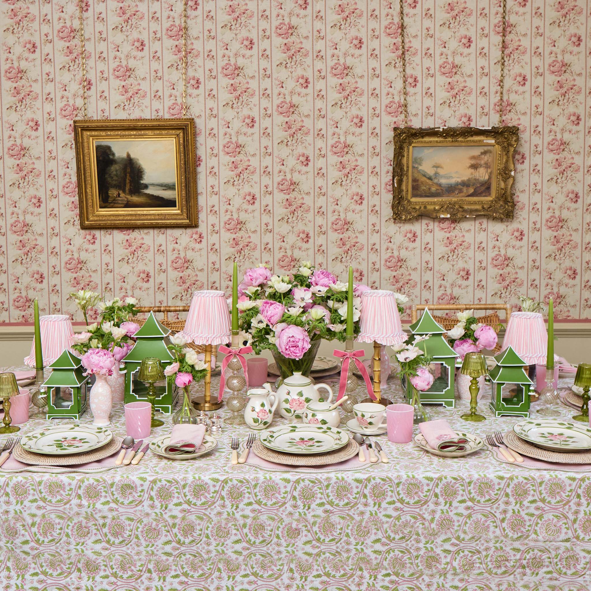 Decorative table setting with floral arrangements, teapots, and pastel colors against a floral wallpapered wall.