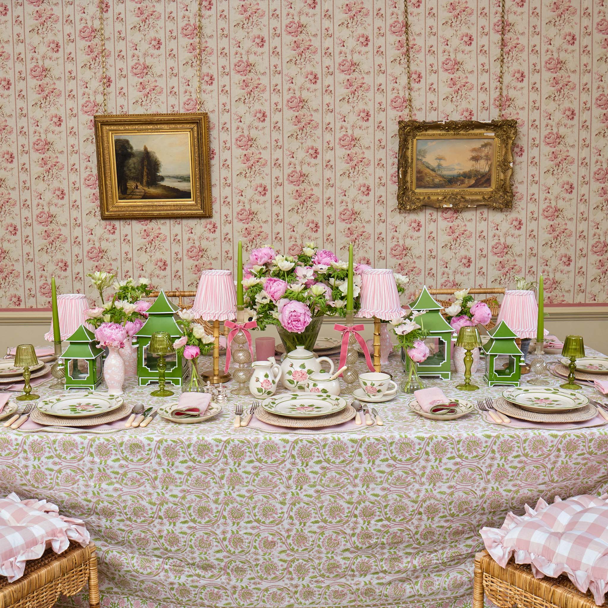 Decorative table setting with floral arrangements, teacups, and green lanterns in a room with floral wallpaper.