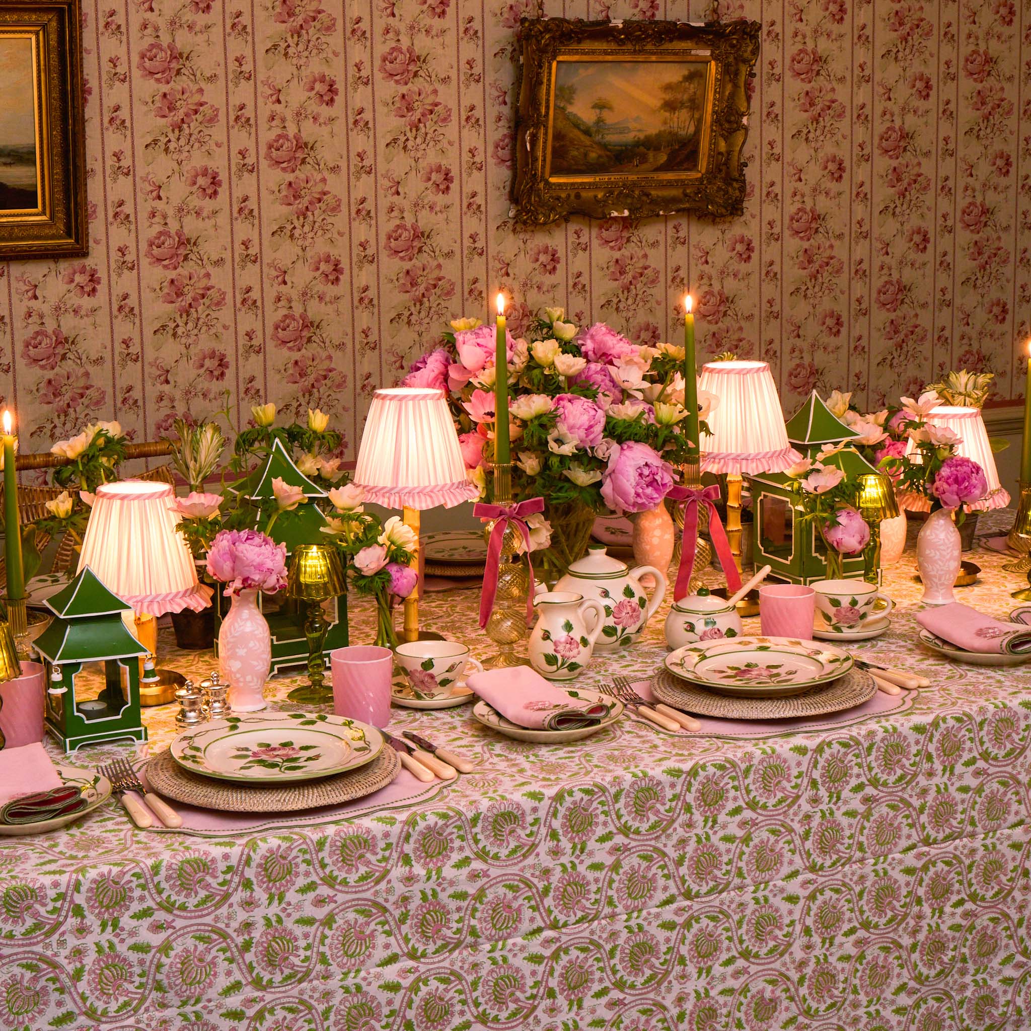 Decorative table setting with floral arrangements, candles, and patterned tablecloth in a room with floral wallpaper.