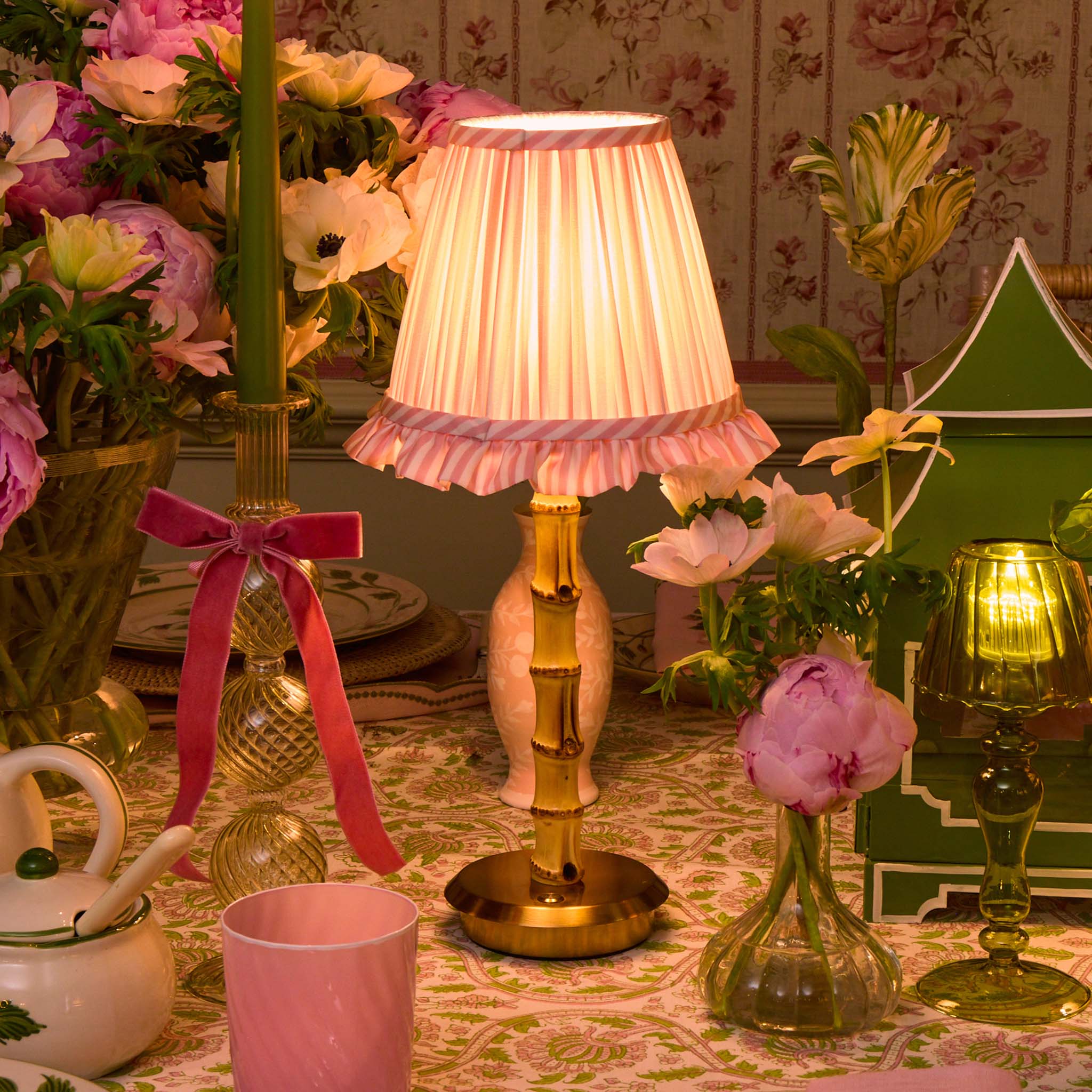 Decorative table setting with a lamp, flowers, and candles on a patterned tablecloth.