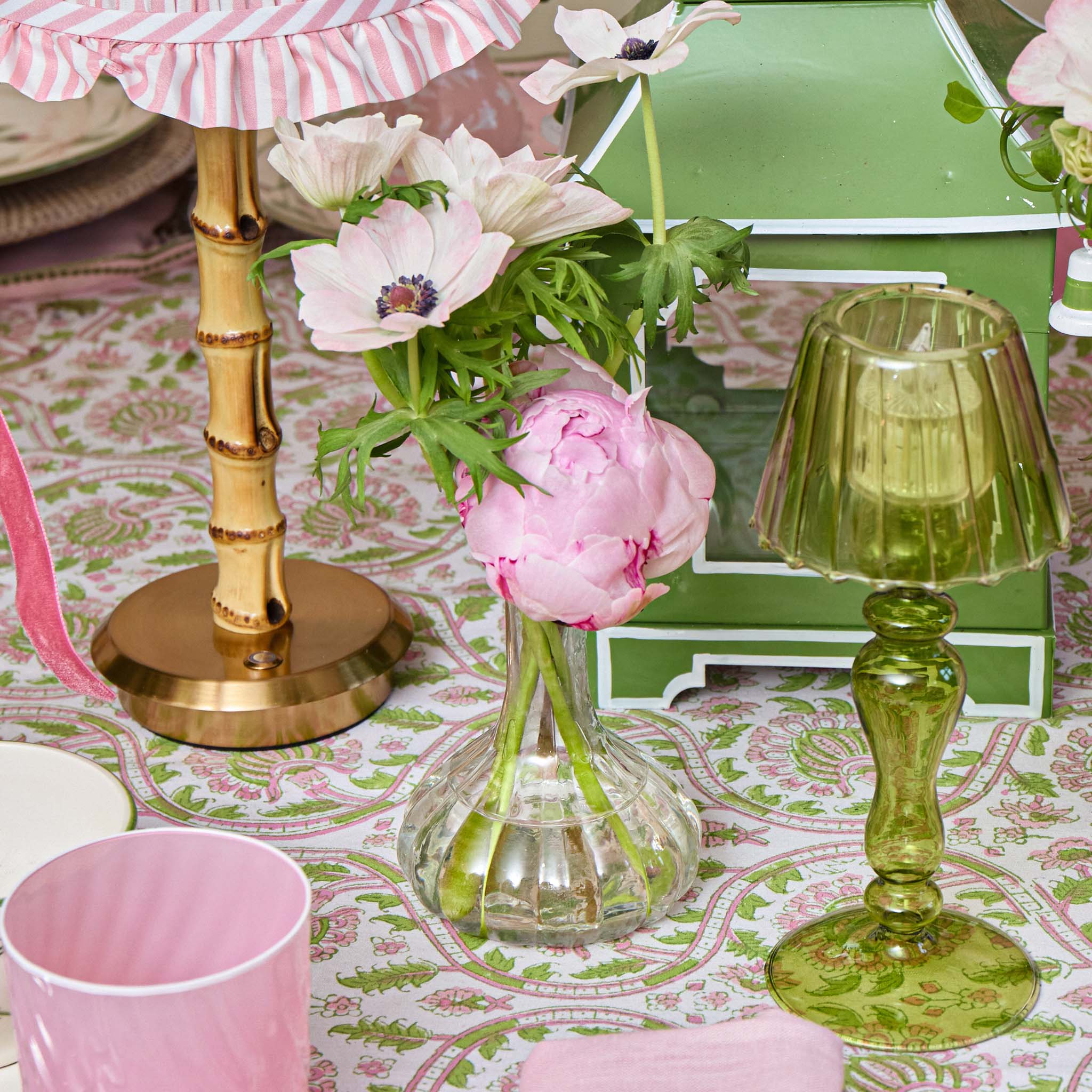 Decorative table setting with flowers, lamps, and a green box on a patterned tablecloth.