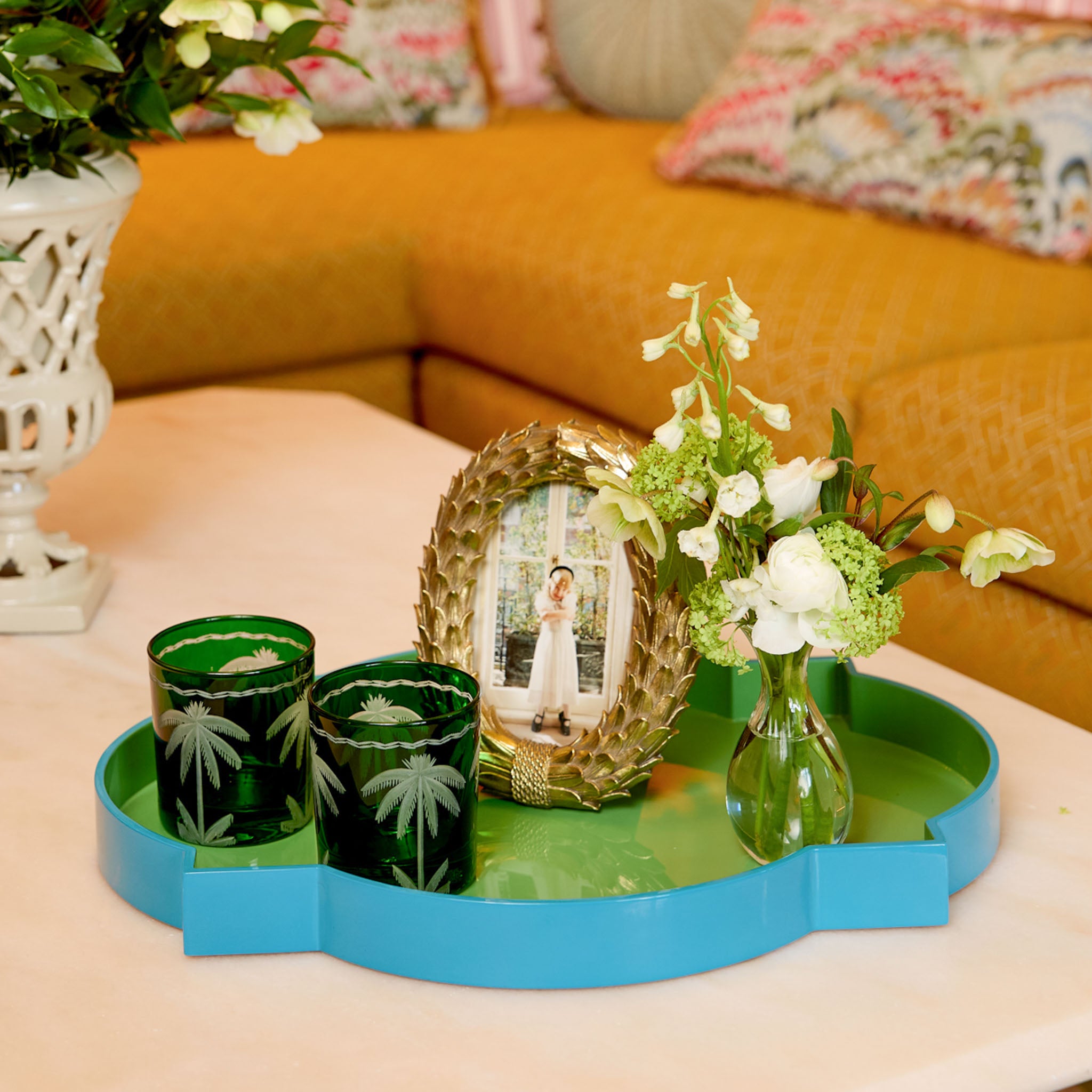 Decorative tray with green candles, a photo frame, and flowers on a table in a living room.