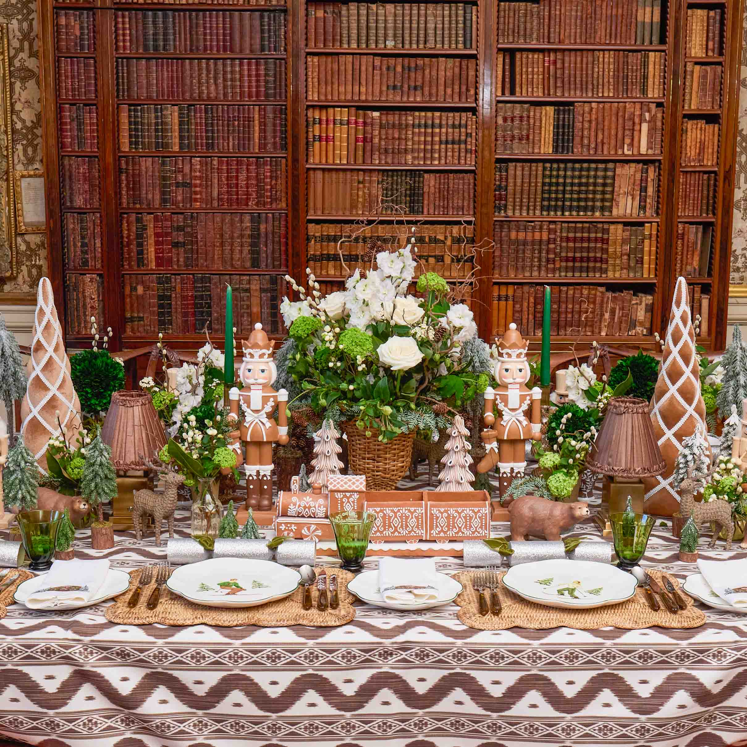 Decorative table setting with gingerbread men, greenery, and candles against a bookshelf background.