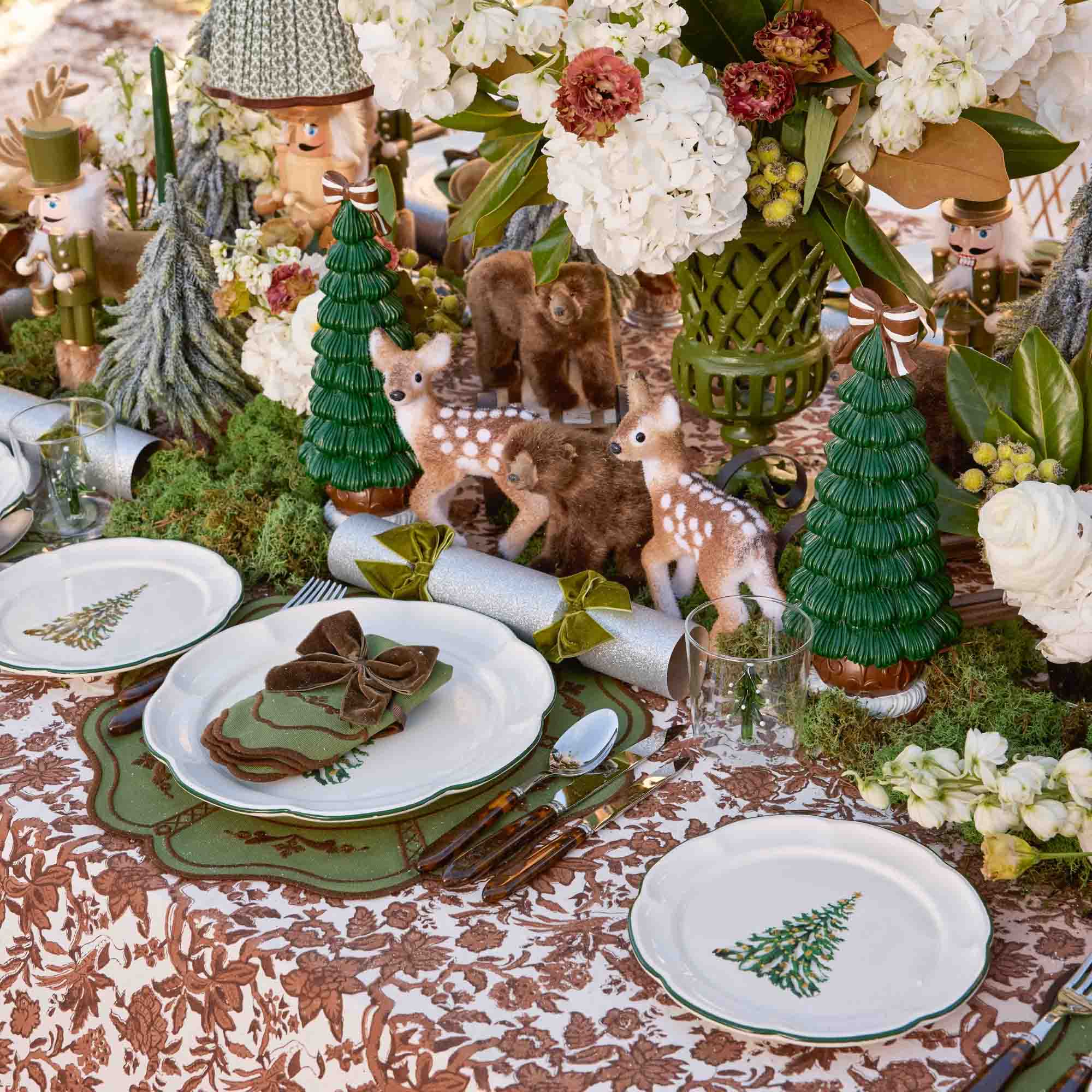 Woodland-themed table setting with deer figurines, floral arrangements, and decorative elements on a patterned tablecloth.