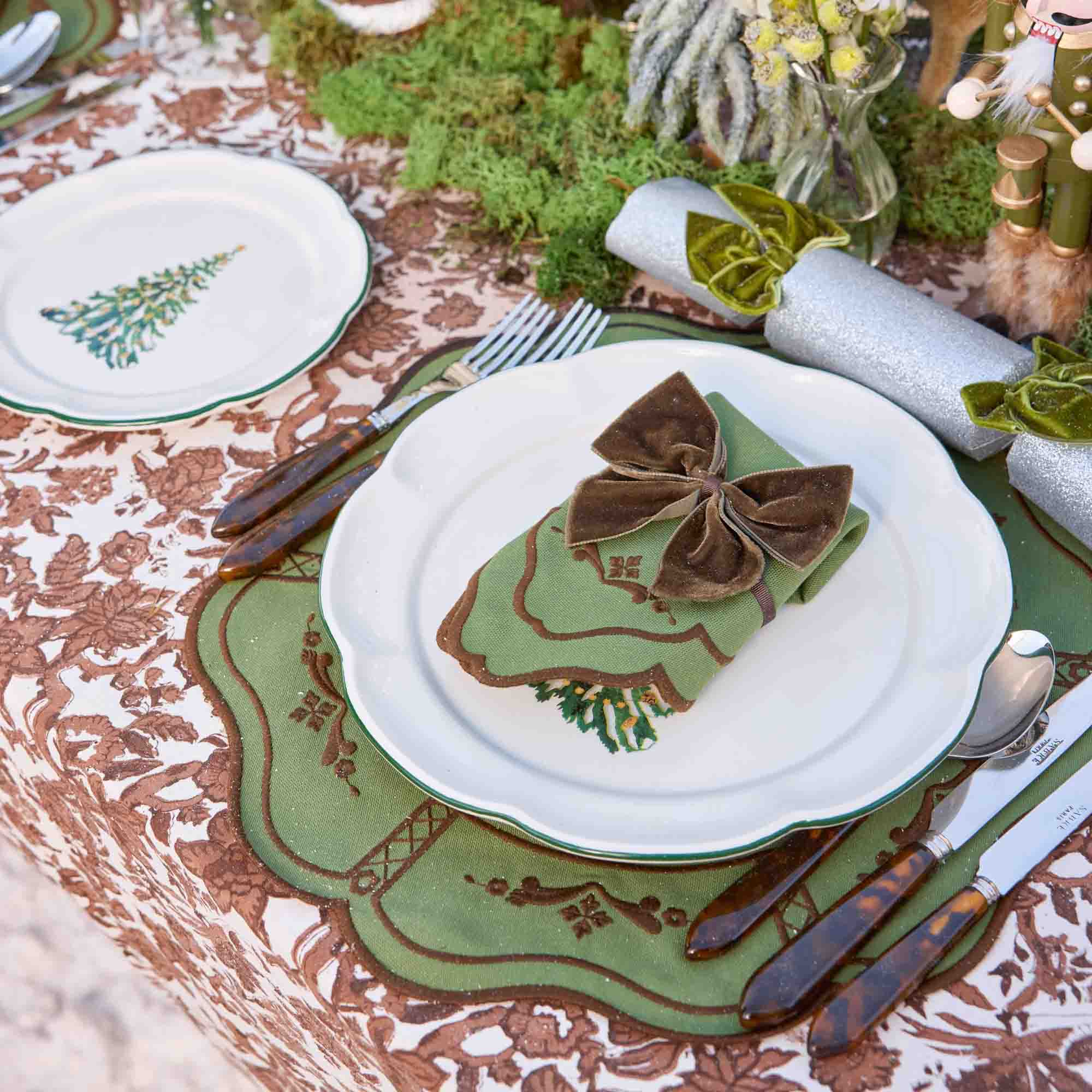 Decorative table setting with green and brown theme, including plates, cutlery, and napkins.
