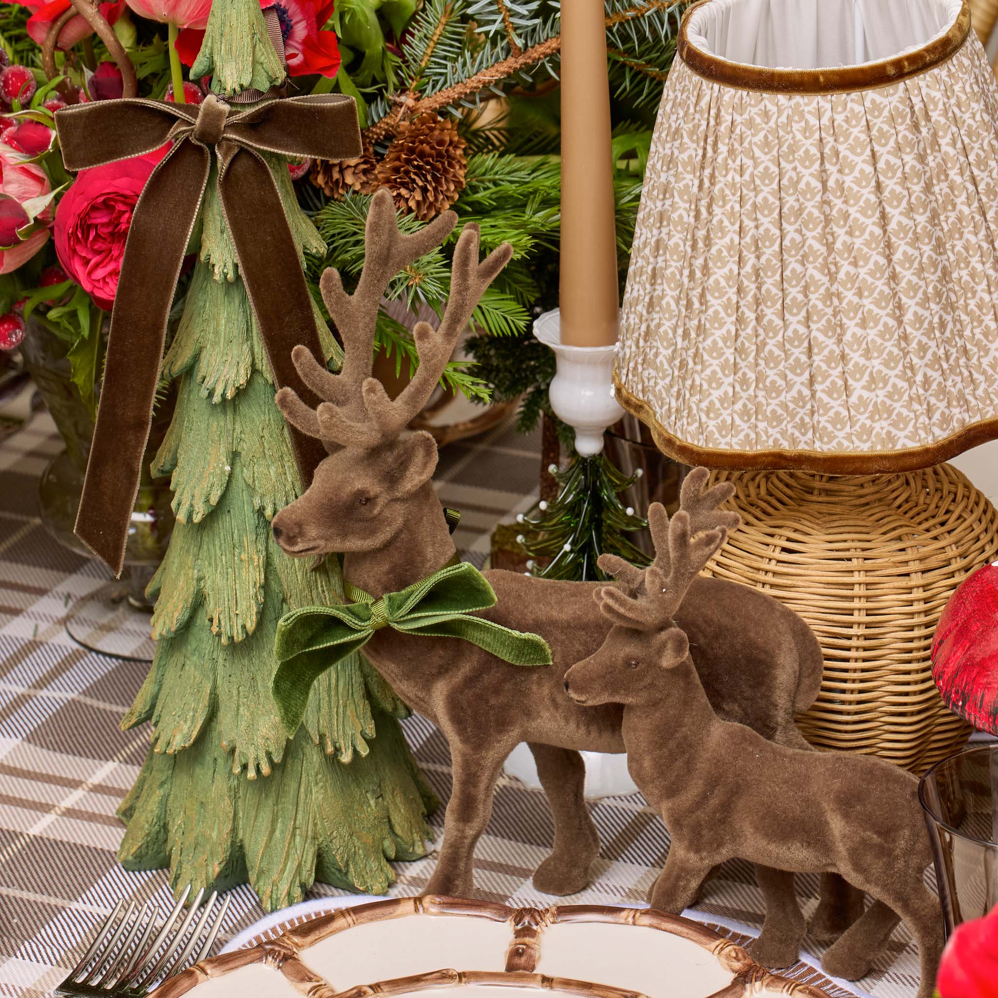 Decorative table setting with reindeer figurines, a small Christmas tree, and a lamp.