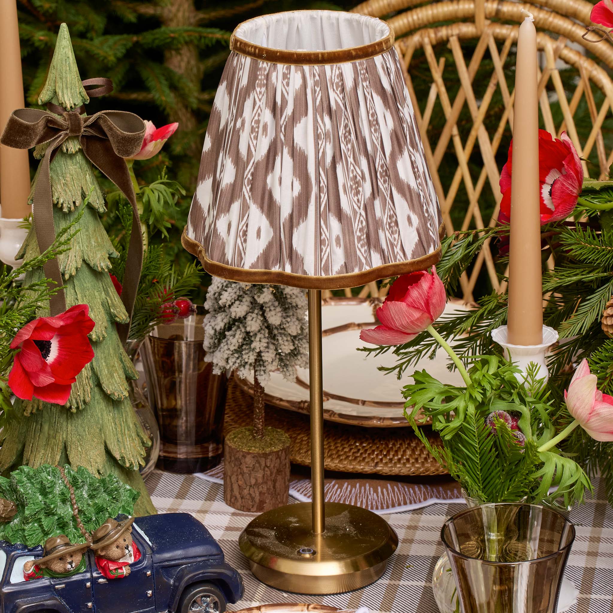Decorative table setting with a lamp, Christmas tree figurine, and floral arrangements.