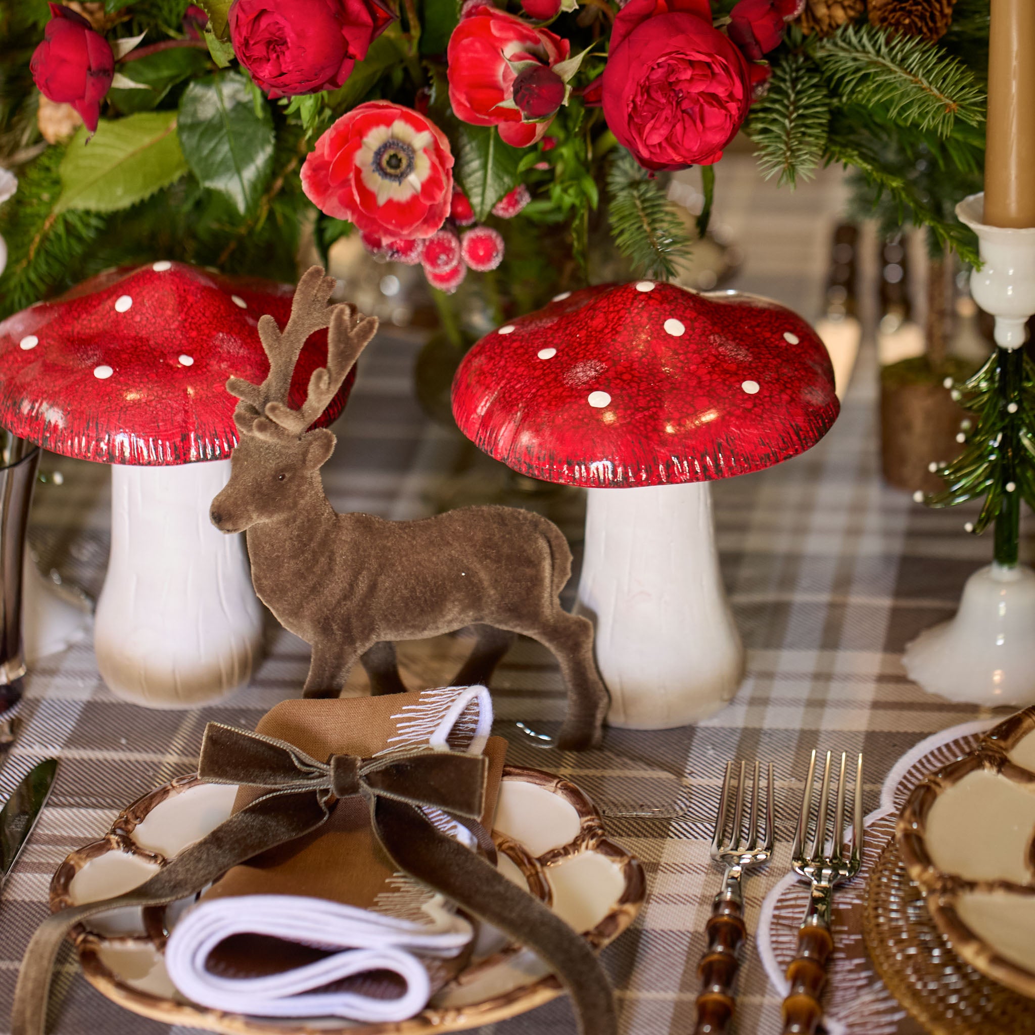 Decorative xmas table setting with red mushrooms, deer figurine, and plaid tablecloth.