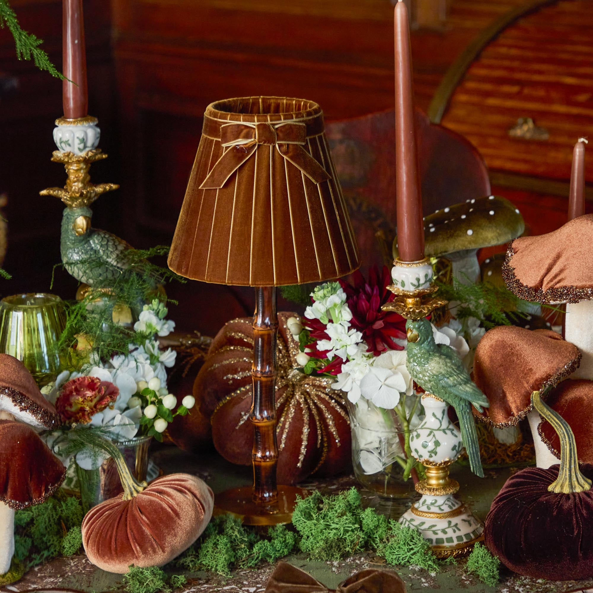 Decorative table setting with a lamp, candles, and pumpkins in a warm, autumnal theme.