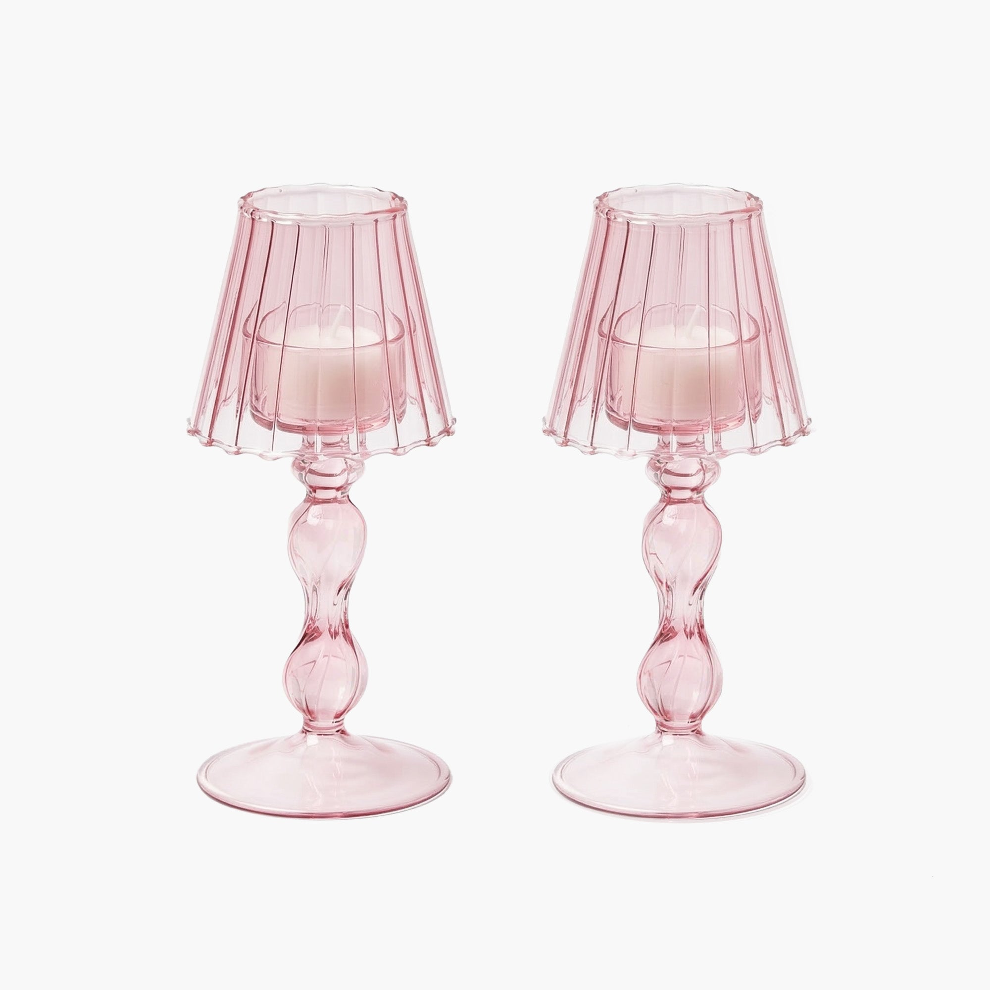 A pair of pink glass lantern tea light holders with a pleated design on the lantern part, placed on a solid surface.