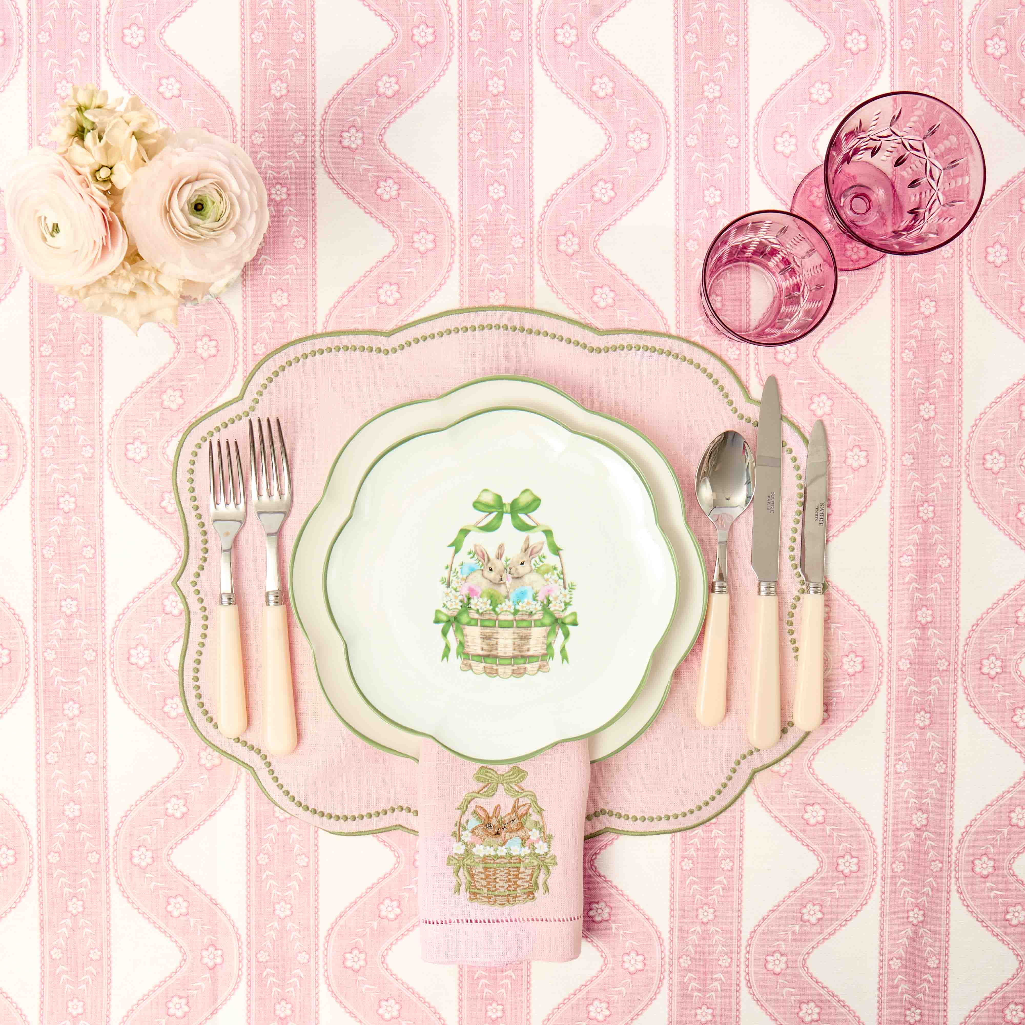 Easter-themed table setting with pink and white striped tablecloth, decorative plates, and floral arrangements.