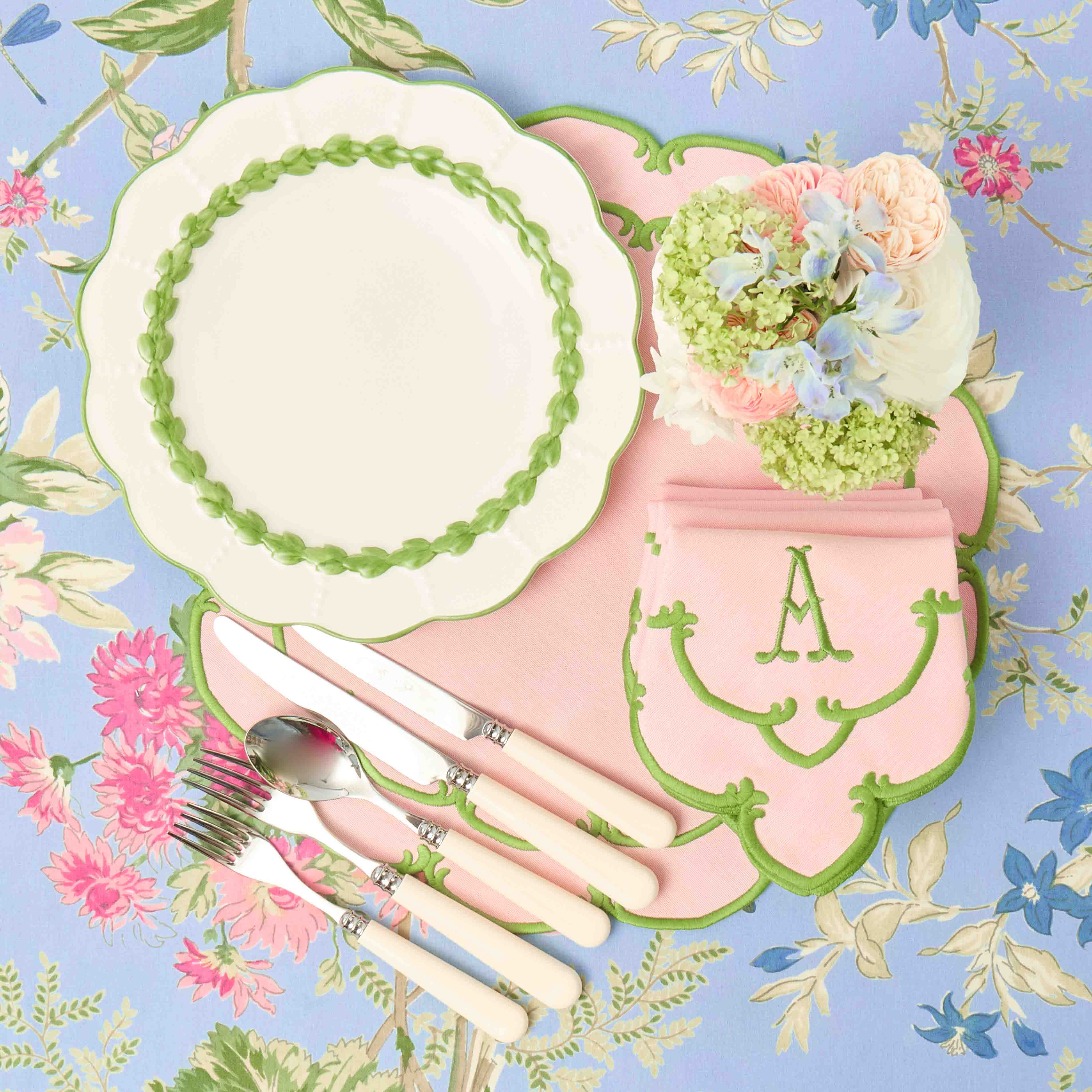 Vintage-style table setting with pink cutlery, floral centerpiece, and decorative plates on a floral-patterned background.
