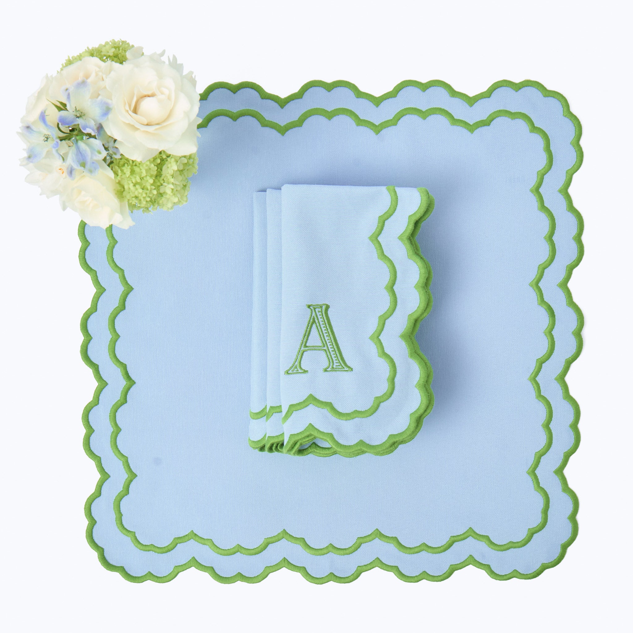 Light blue plate with green rim and monogram 'A', accompanied by white flowers.