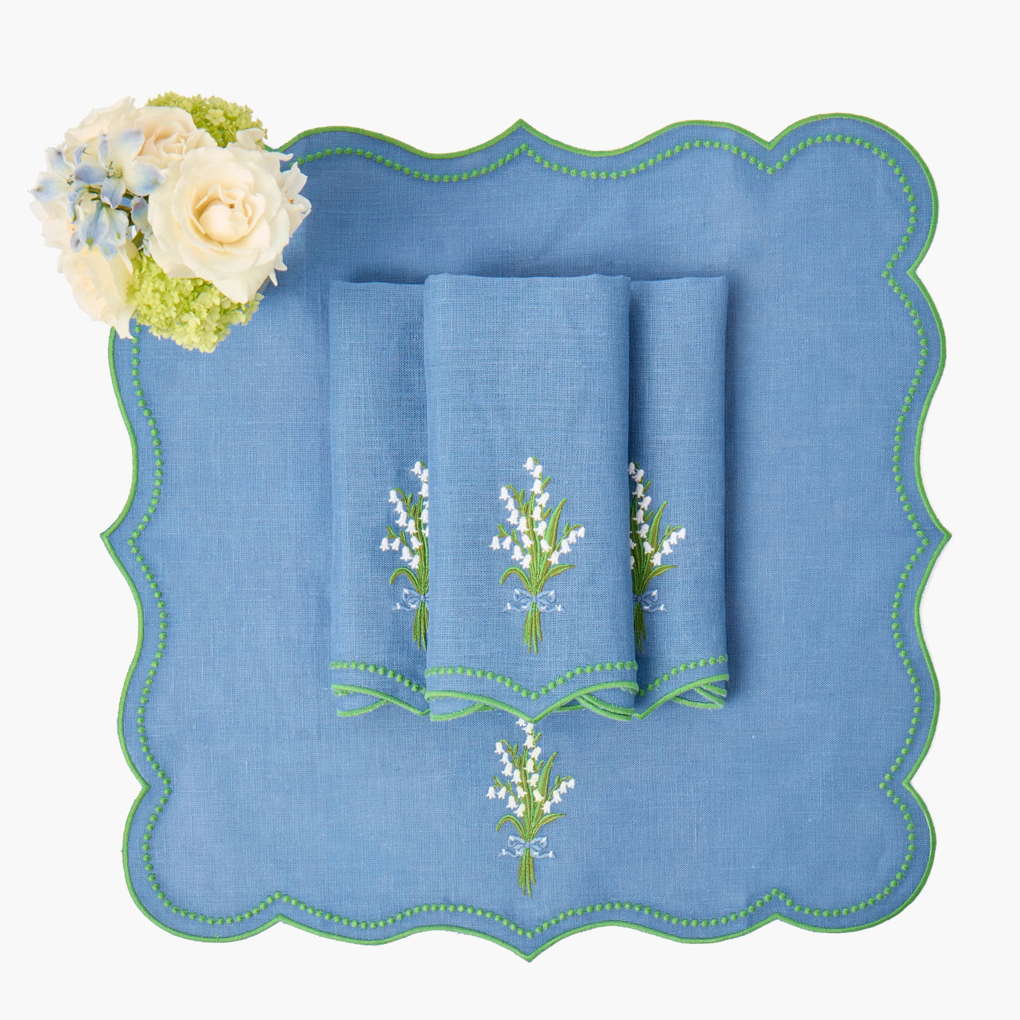 Set of blue towels with floral embroidery on a matching blue placemat, accompanied by a bouquet of flowers.