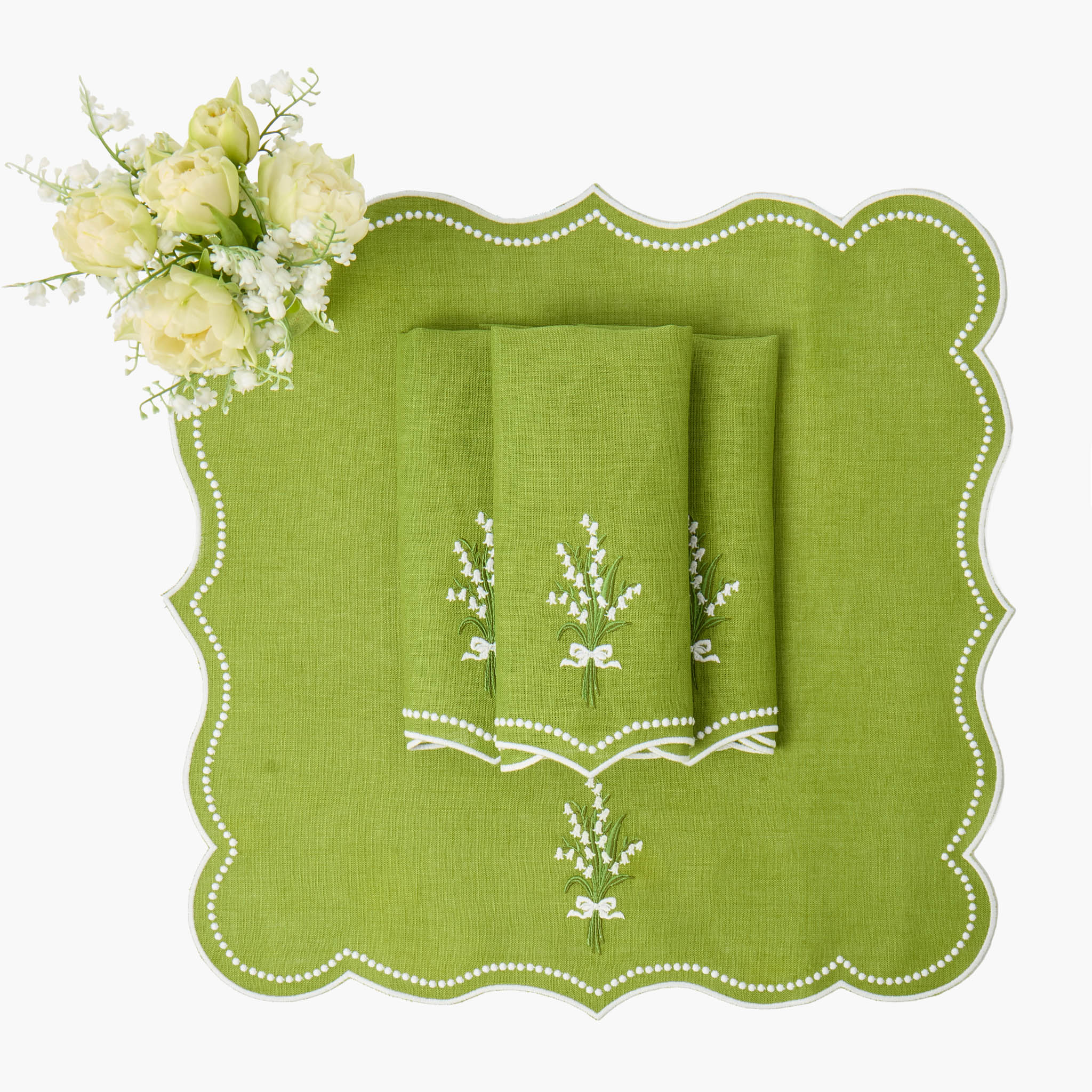 Green embroidered placemat with folded napkins and white flowers on a white background