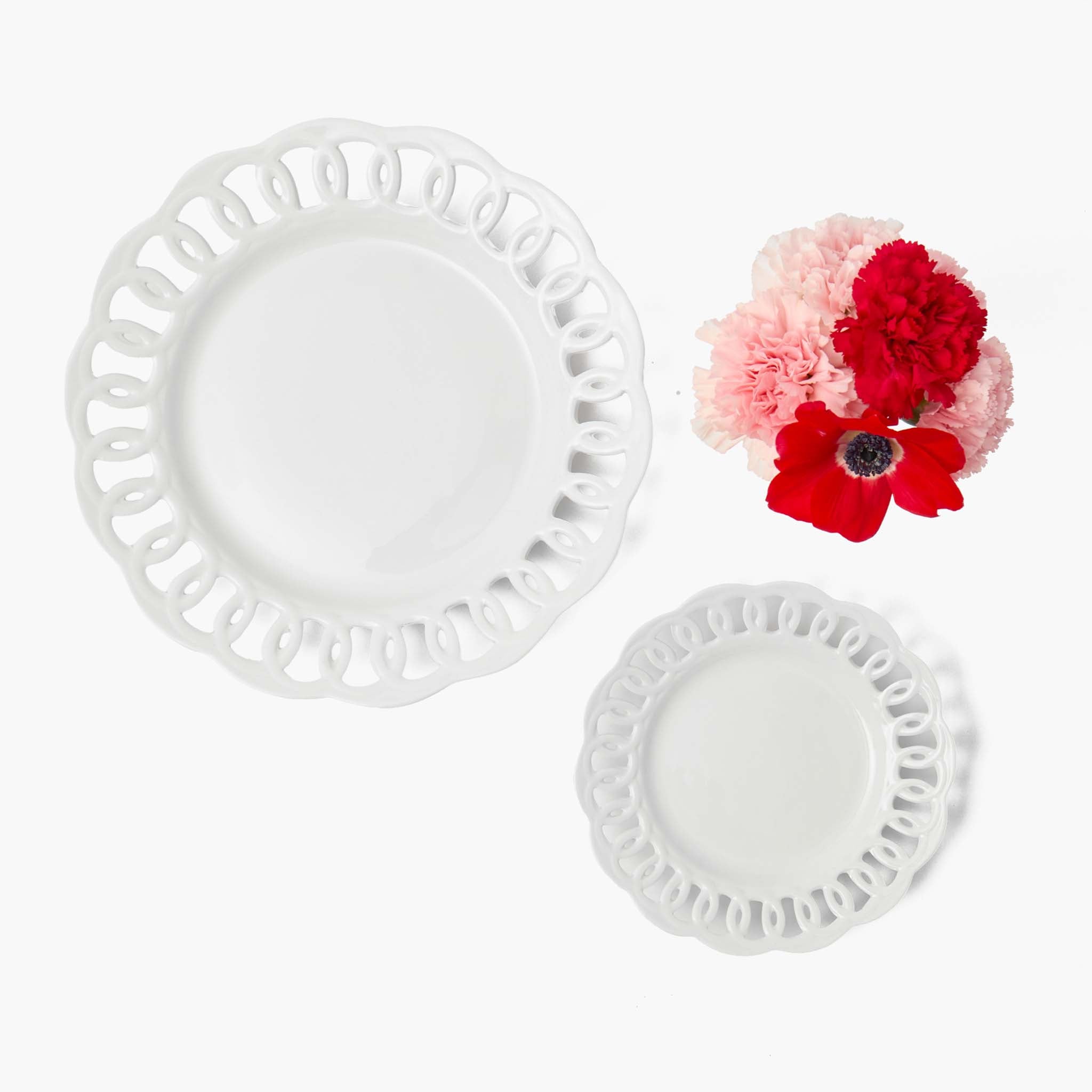Two white decorative plates with lace edges on a white background, accompanied by pink and red flowers.