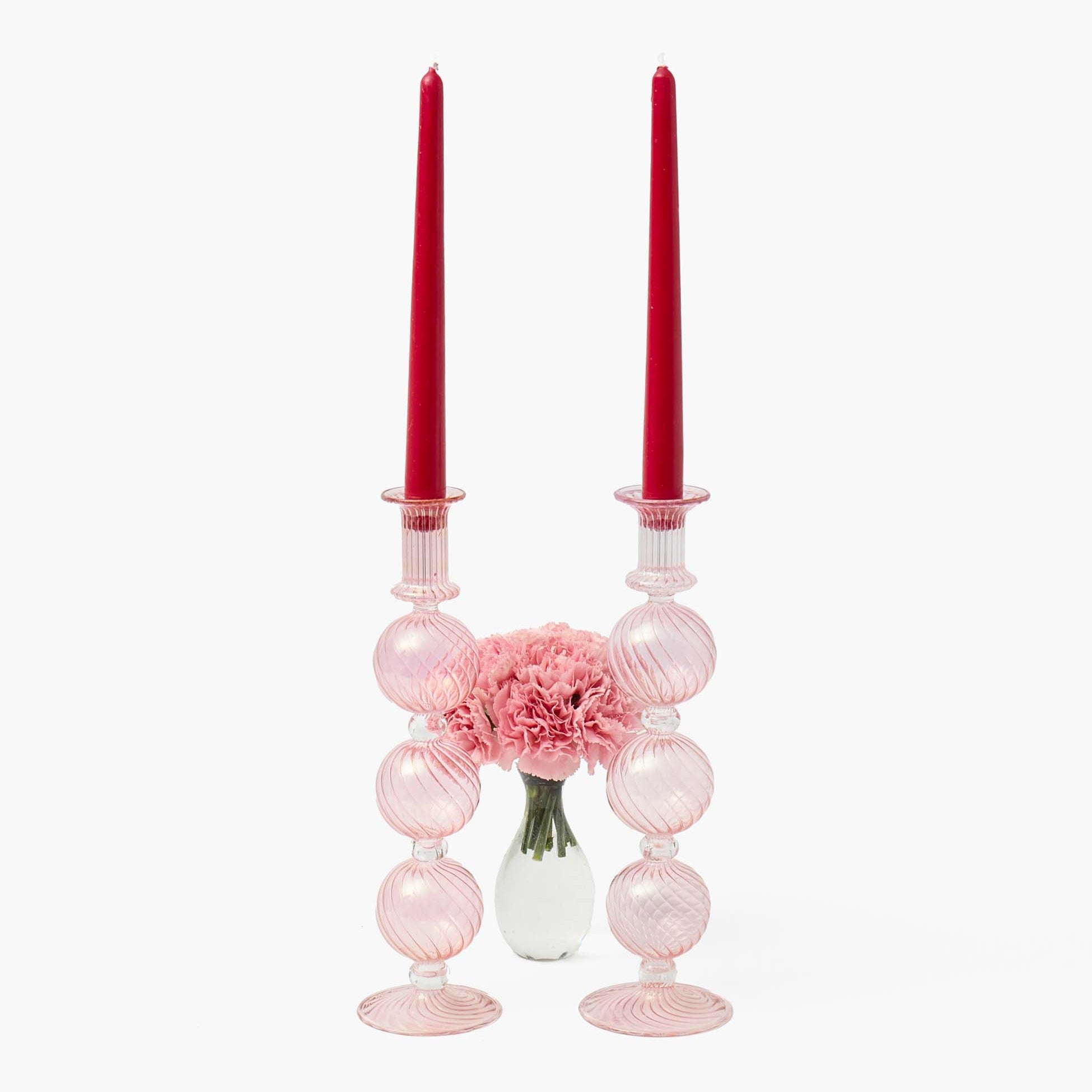 Pink candle holders with red candles and a vase of pink flowers on a white background