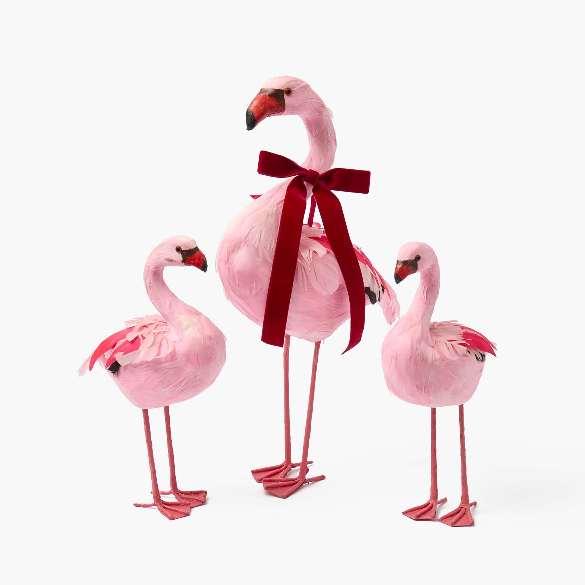 Three pink flamingo figurines with a red bow on a white background