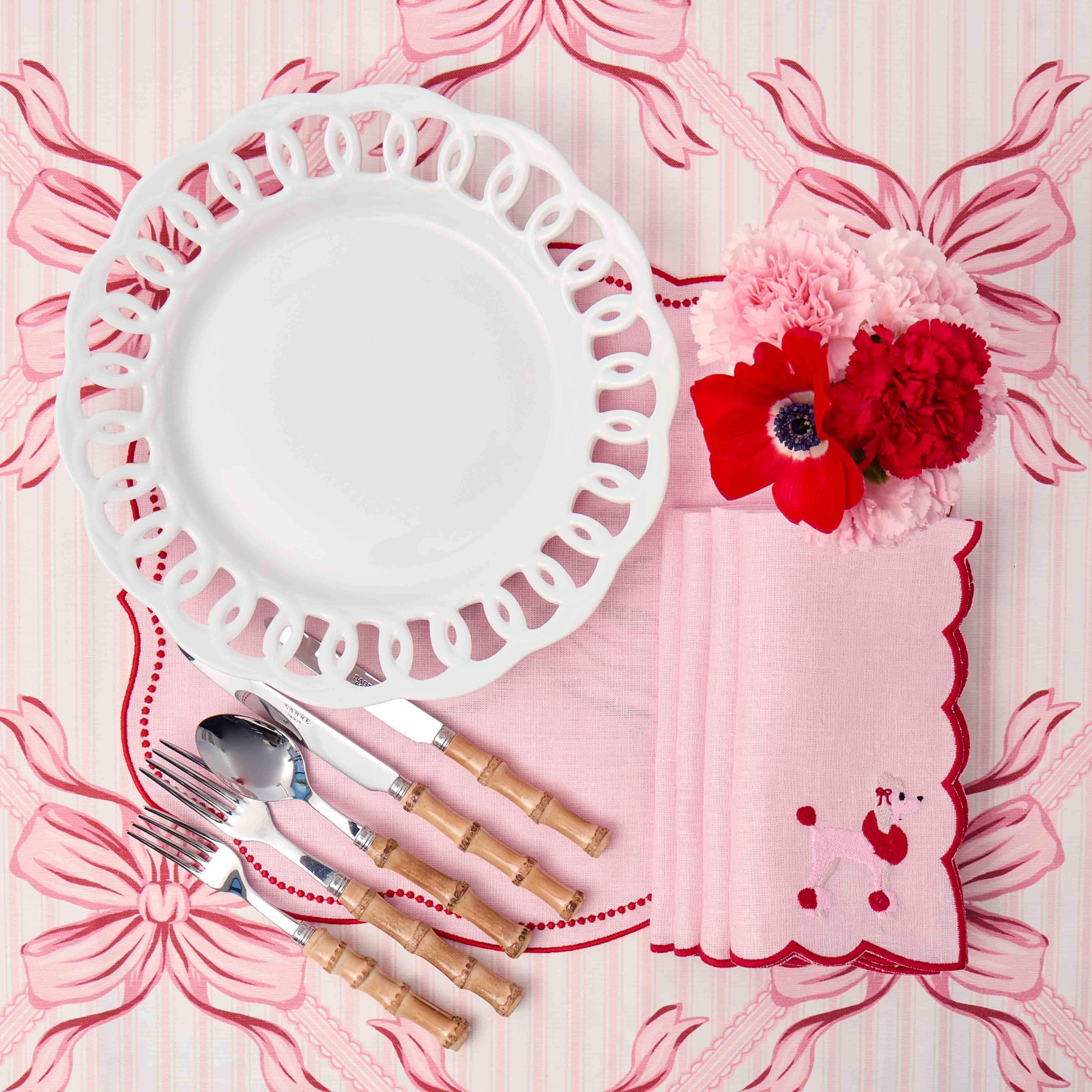 Decorative table setting with a white plate, red flowers, and pink napkin on a matching background.