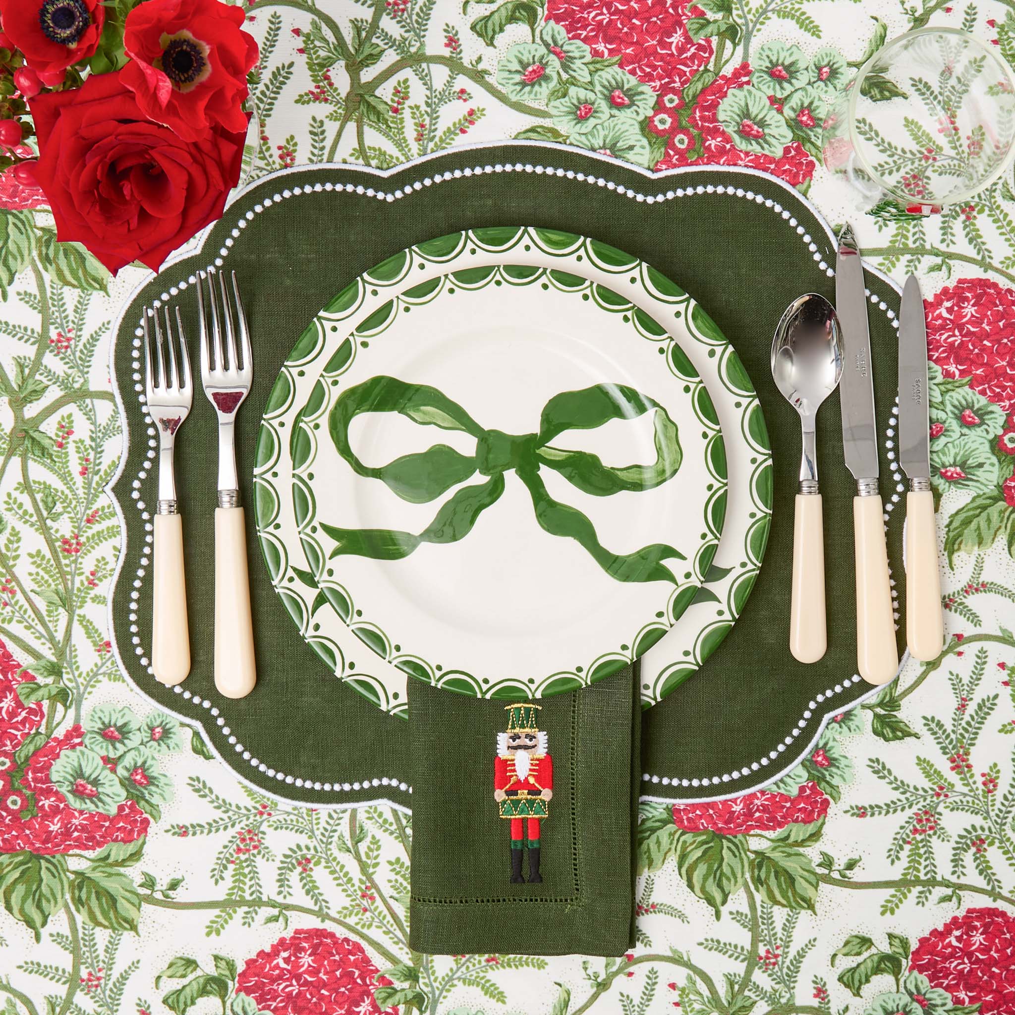 Christmas-themed place setting with green bow plate, floral tablecloth, and decorative napkin.