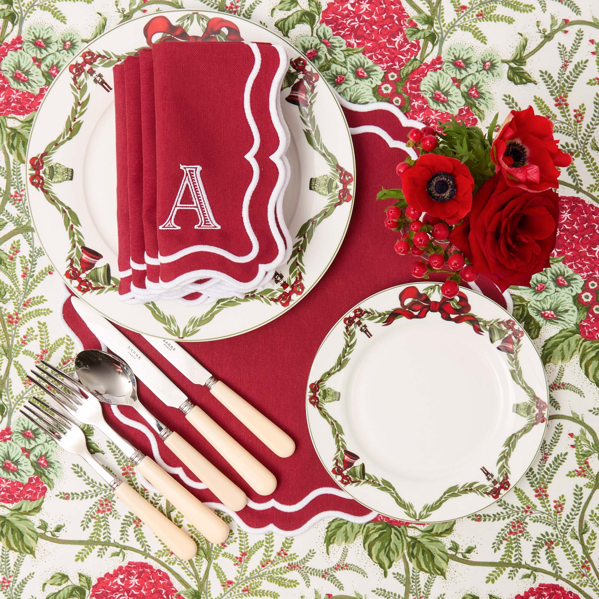 Christmas-themed table setting with red and green decorations, including plates, napkins, and cutlery.