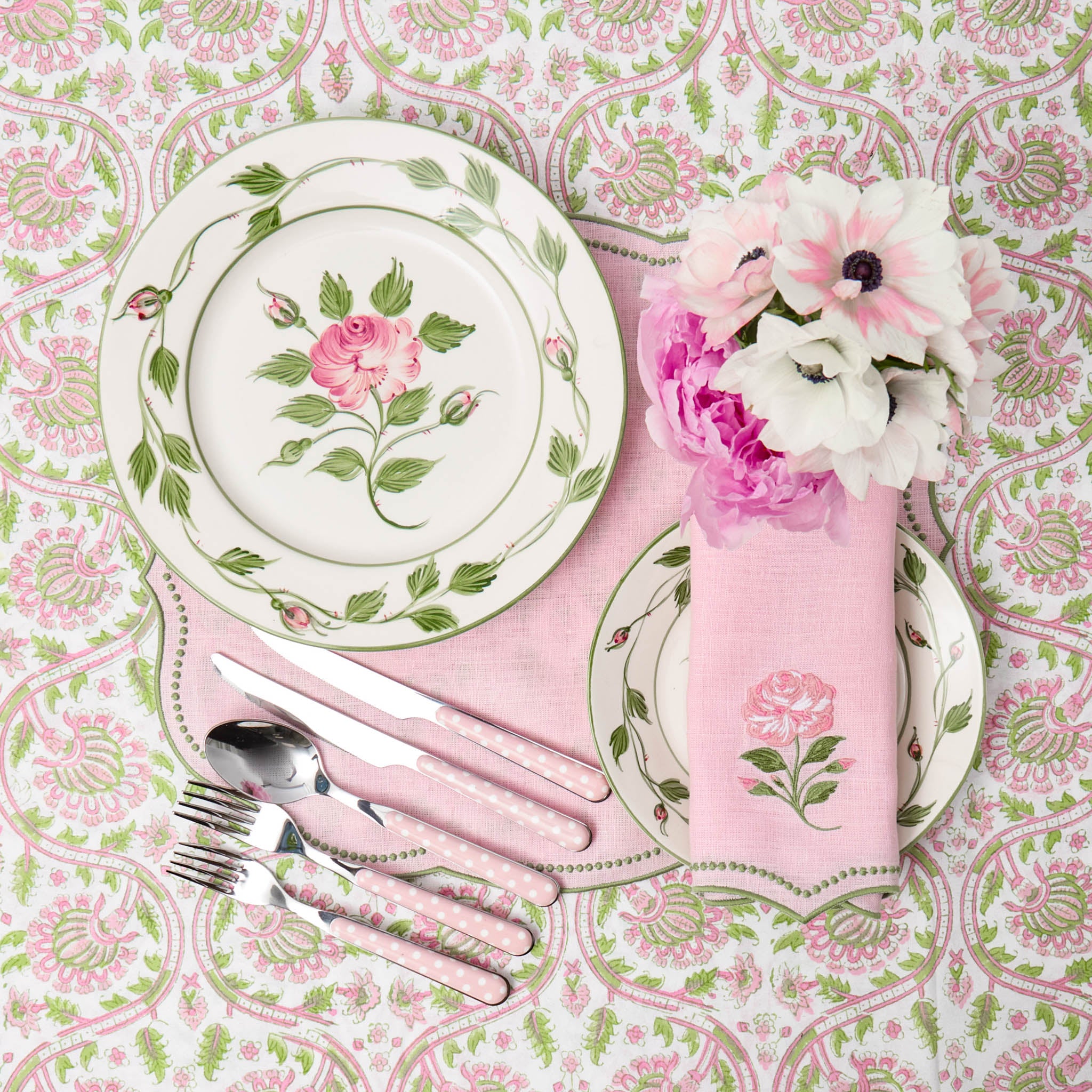 Floral table setting with plates, napkin, and cutlery on a patterned tablecloth.