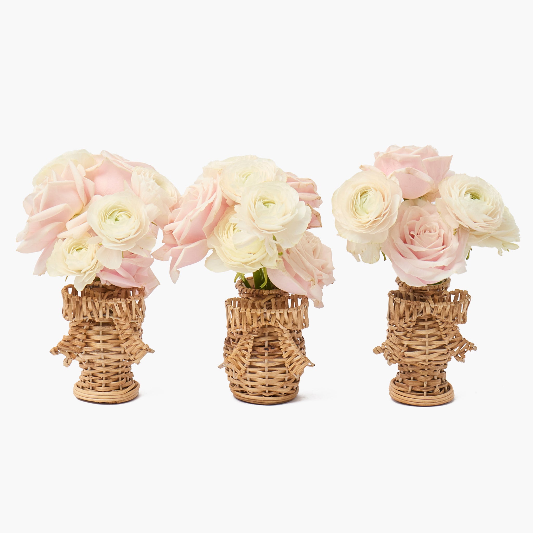 Three wicker vases with pink and white flowers on a white background