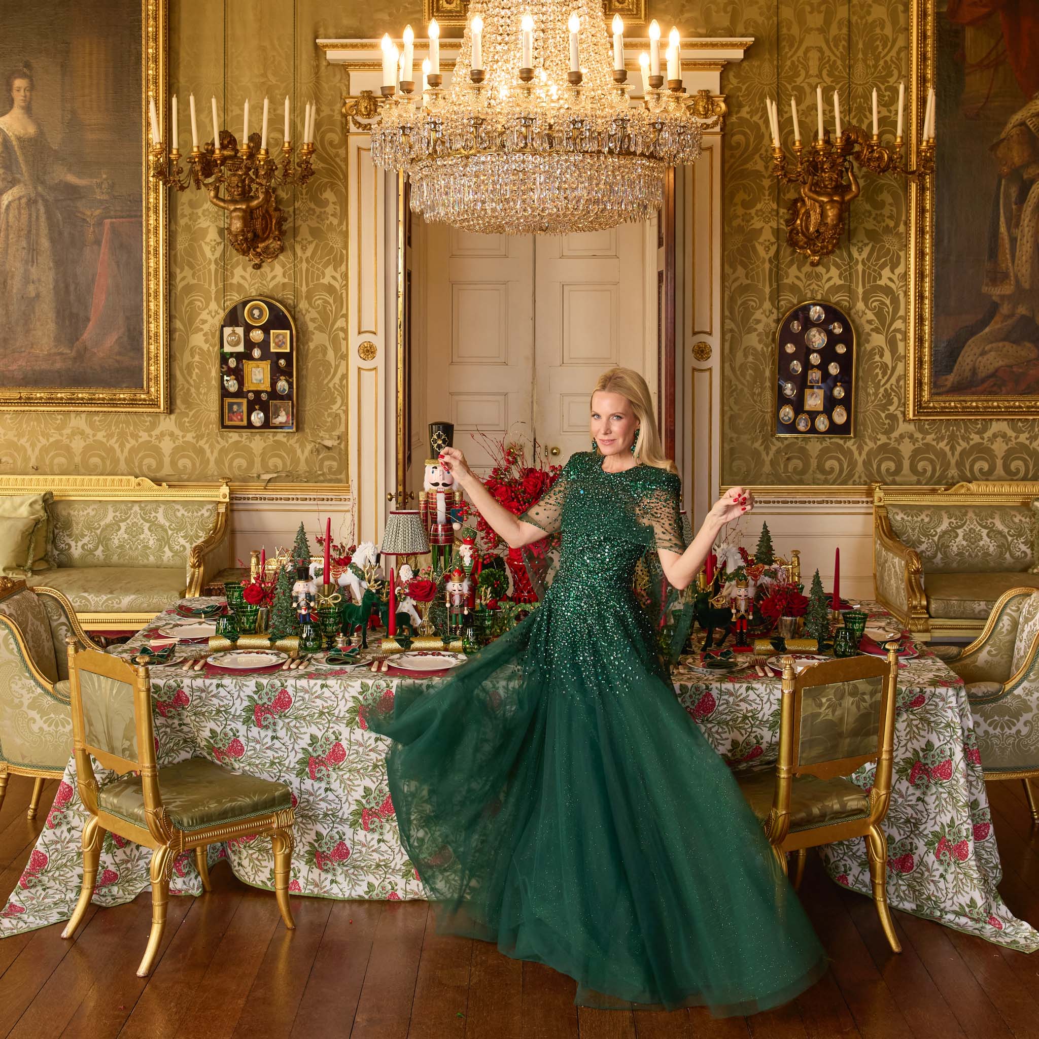 Alice in a green dress standing in an ornate xmas dining room with a large chandelier.