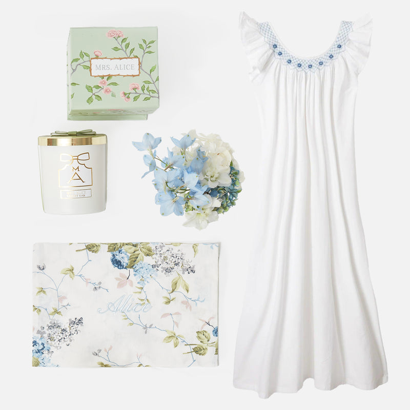Dive into tranquility with the Bonne Nuit Blue Giftscape, featuring an Alice Blue Sleeveless Nightdress, a Velvet Oak Scented Candle, and a Monogrammable Blue Chintz Pochette.