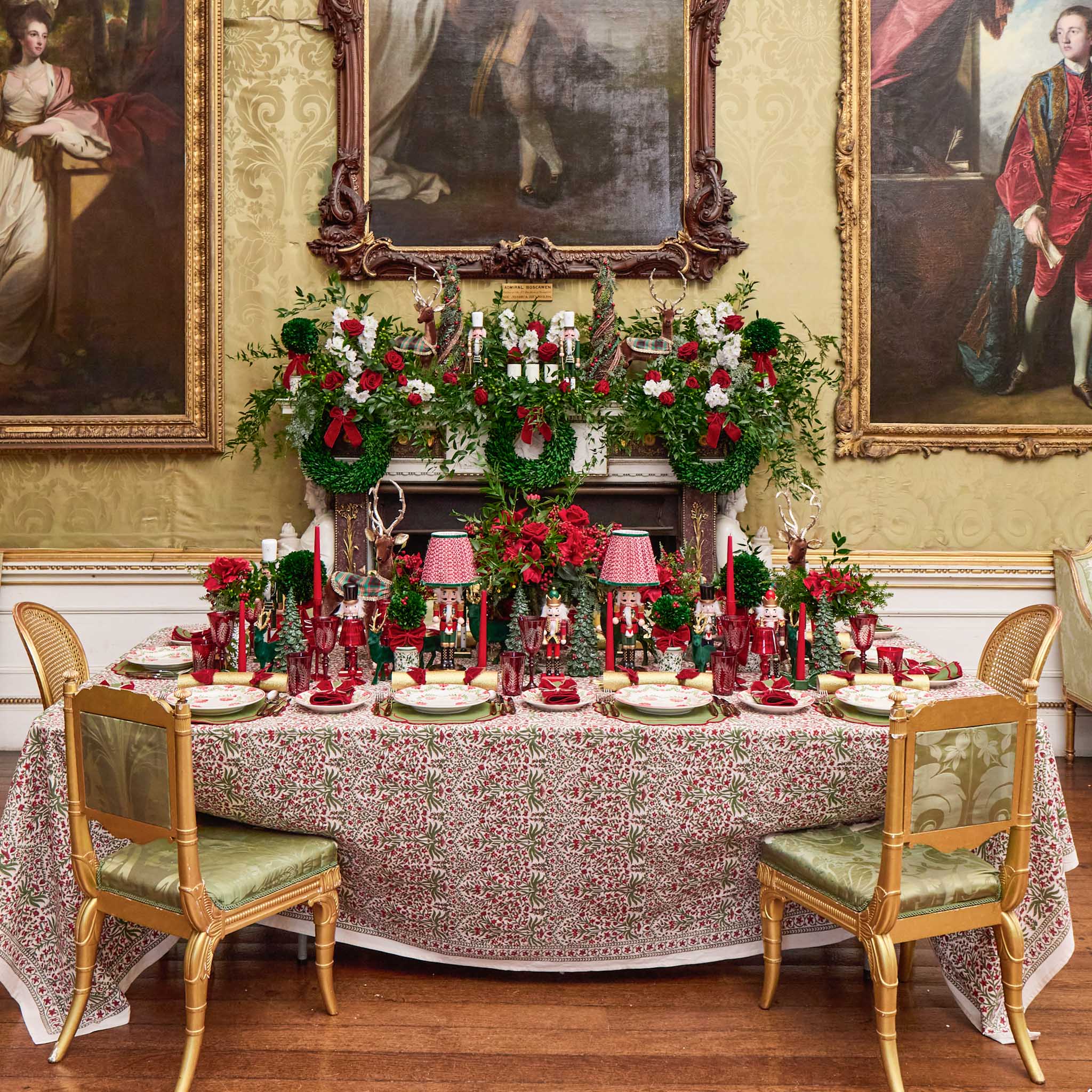 Decorative table setting with floral arrangements and candles in a room with classical paintings on the walls.