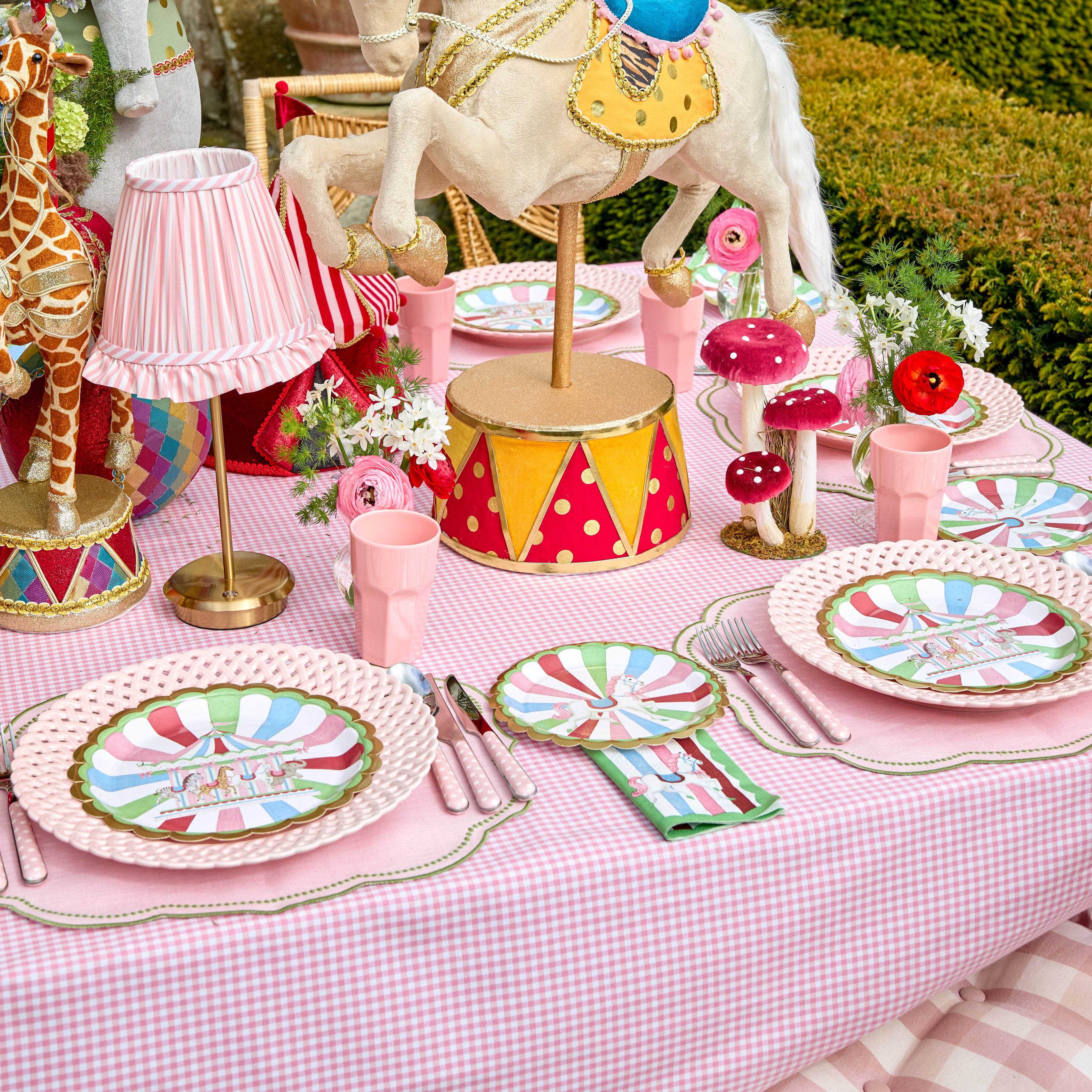 Colorful table setting with carousel-themed decor, including a horse and giraffe figurines, on a checkered tablecloth.