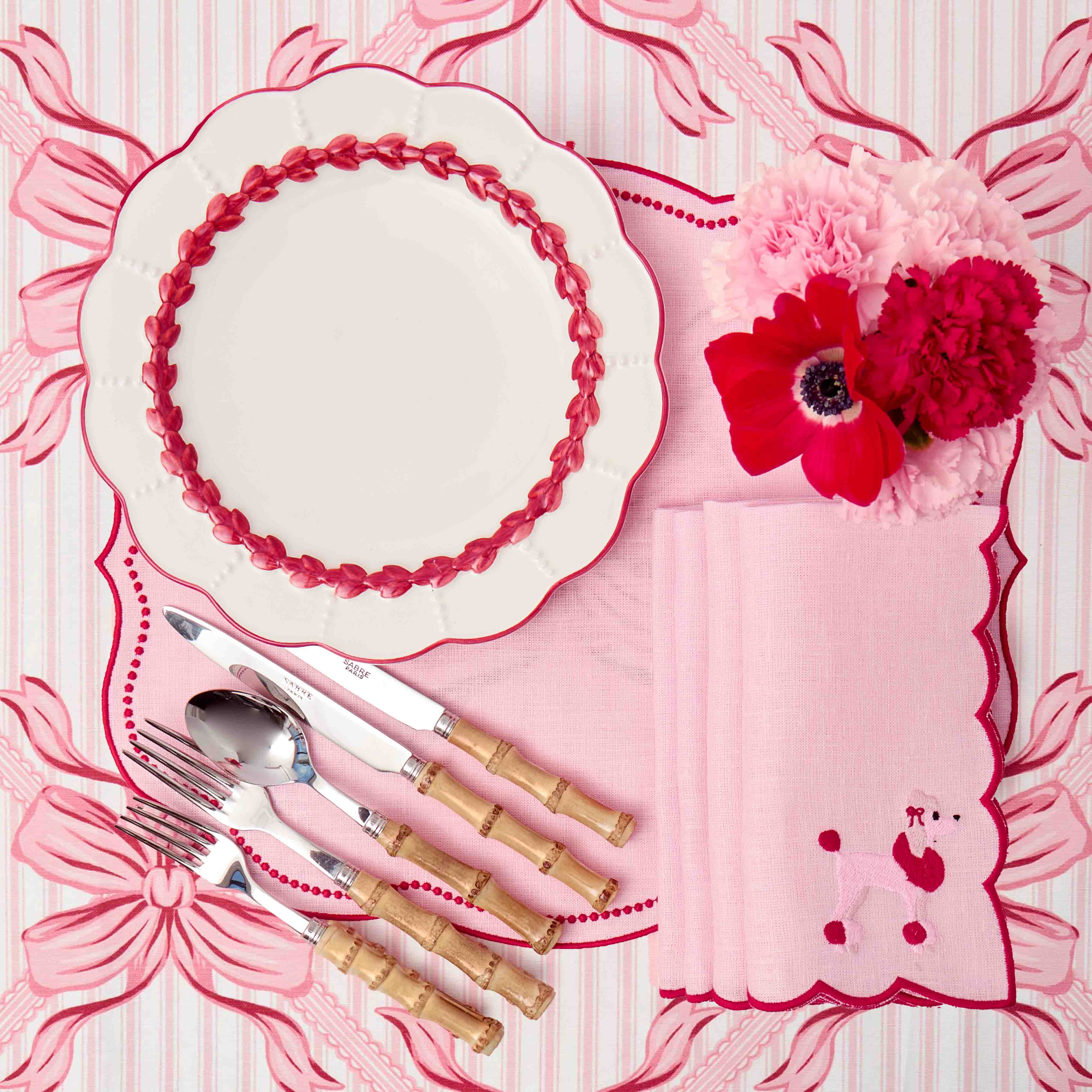 Decorative table setting with pink floral design, white plate, silverware, and red flowers on a matching pink background.