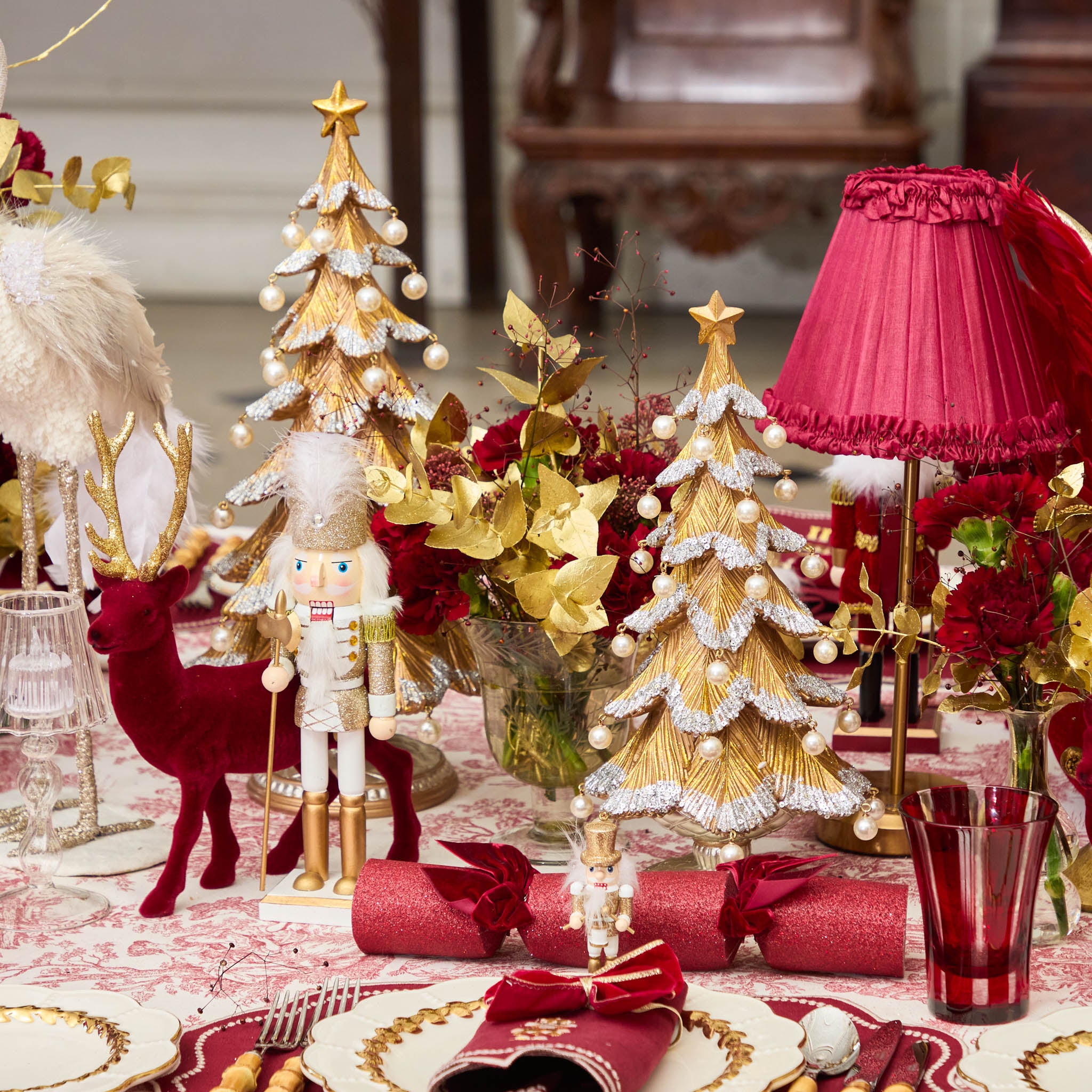 Decorative Christmas table setting with gold trees, red reindeer, and nutcrackers.