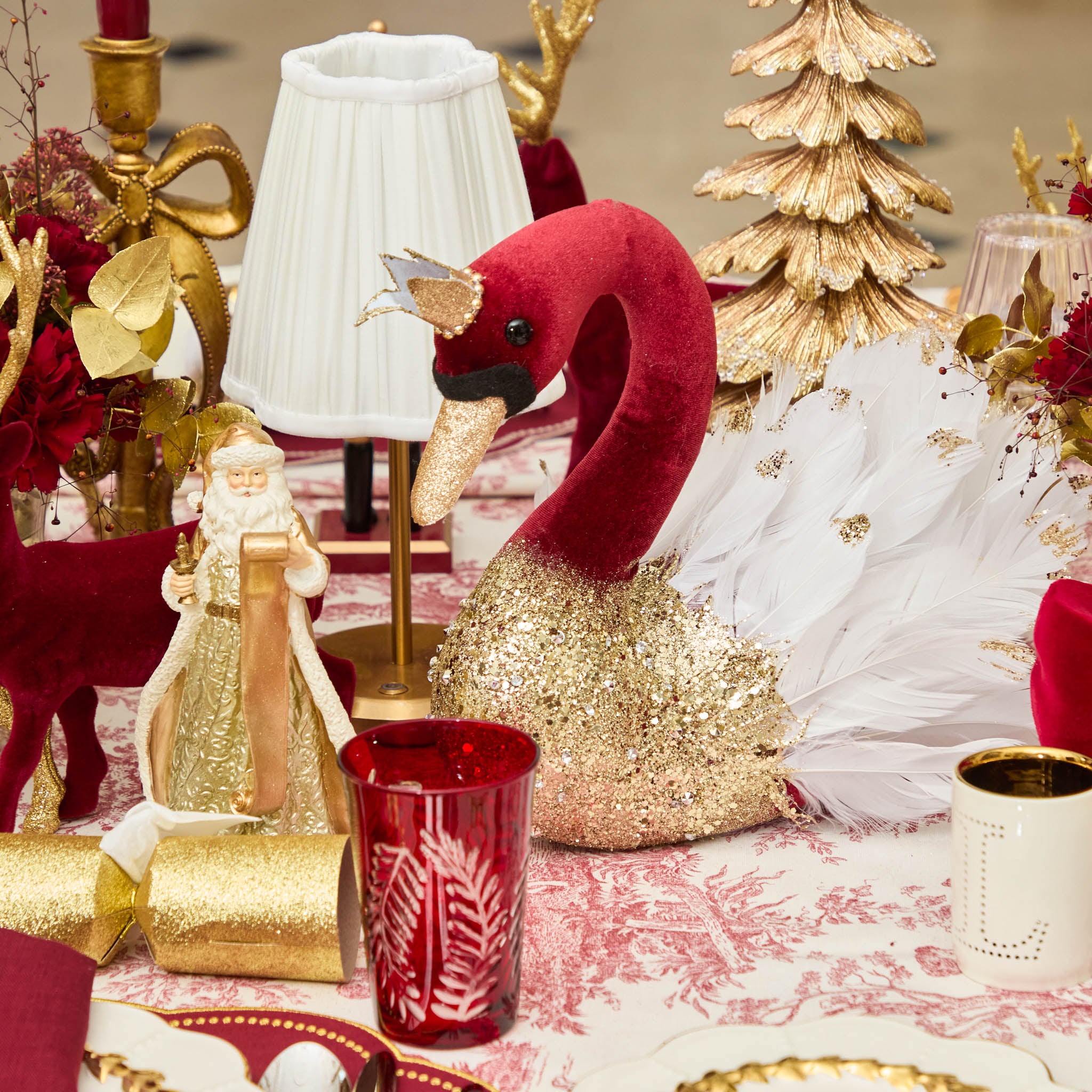 Decorative table setting with a red and gold swan, Christmas trees, and other festive items.