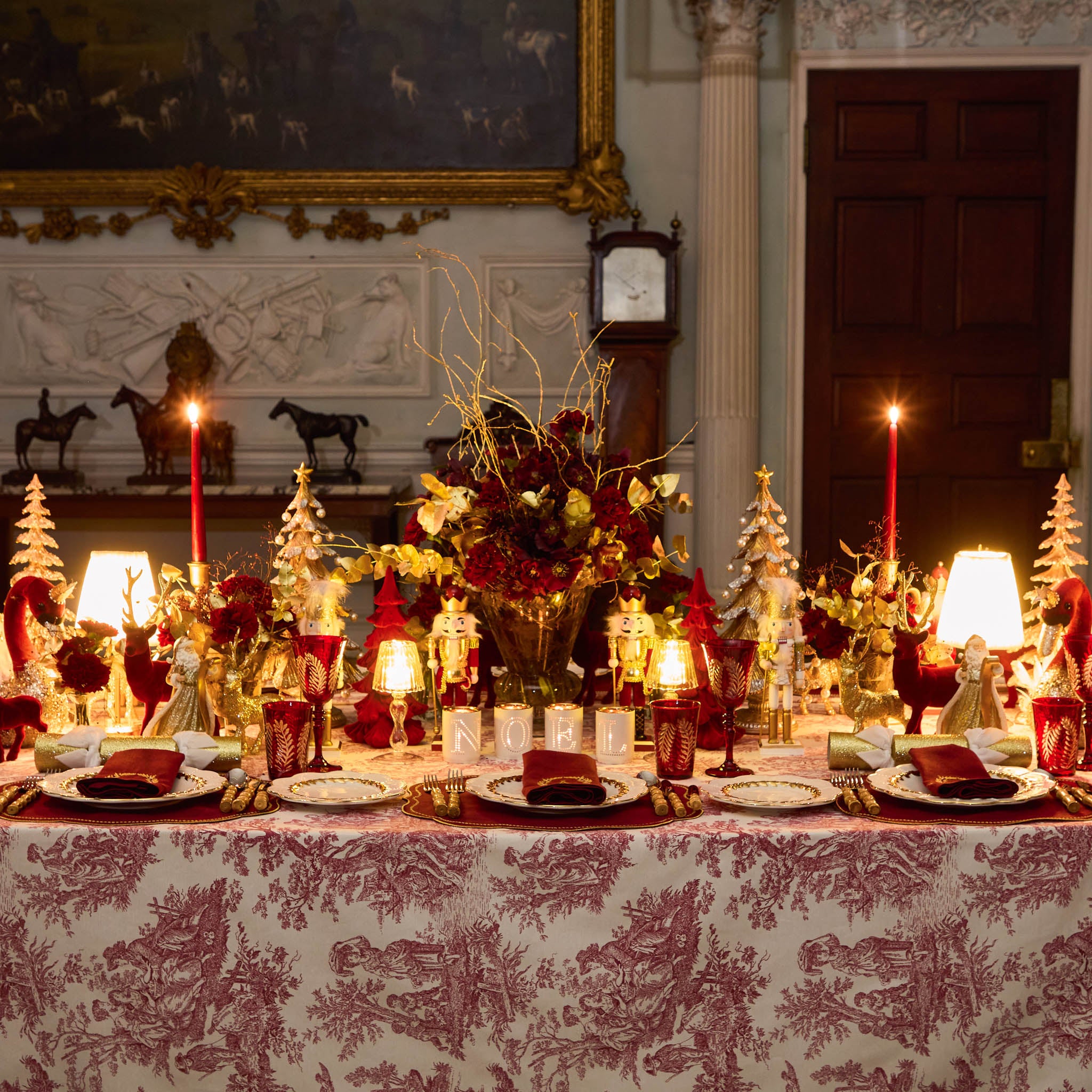 Decorative Christmas table setting with candles, flowers, and small trees in a formal room.