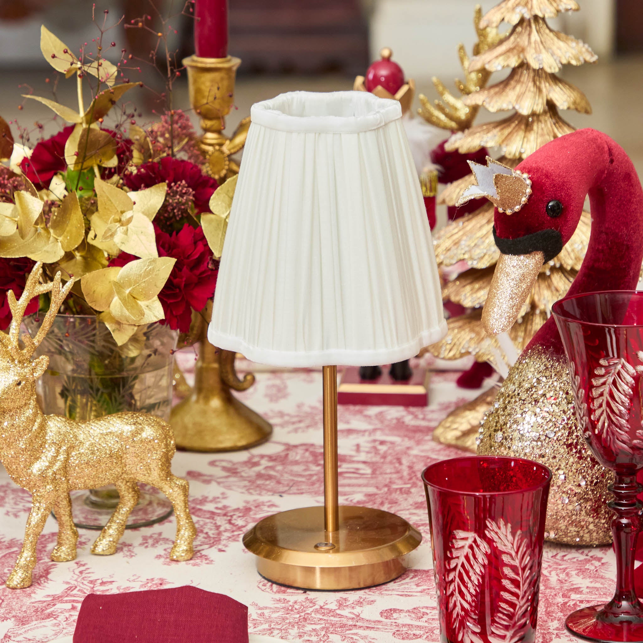 Decorative table setting with a lamp, red glasses, and Christmas-themed decor.